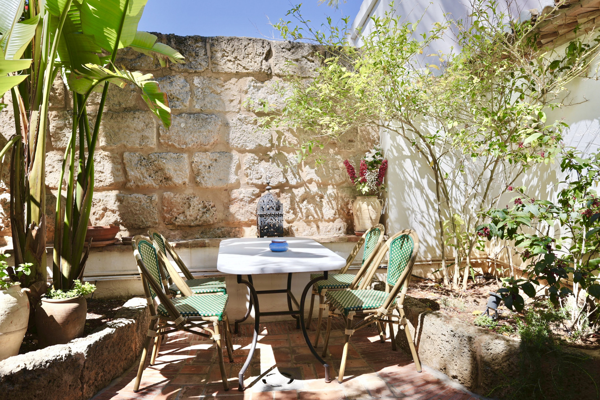 Patio con mesa de mármol, sillas de mimbre y pared de piedra rústica. Ambiente tranquilo y natural.