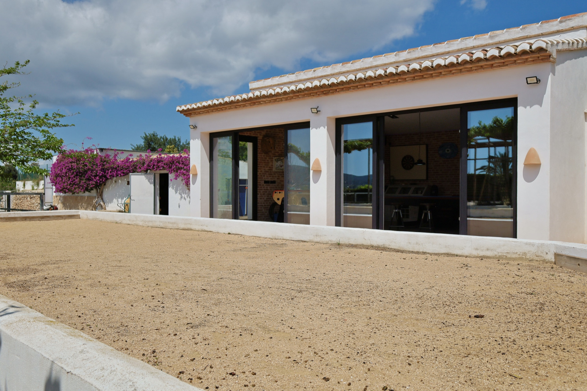 Vista exterior de la villa con cancha de arena y amplios ventanales que reflejan el interior.