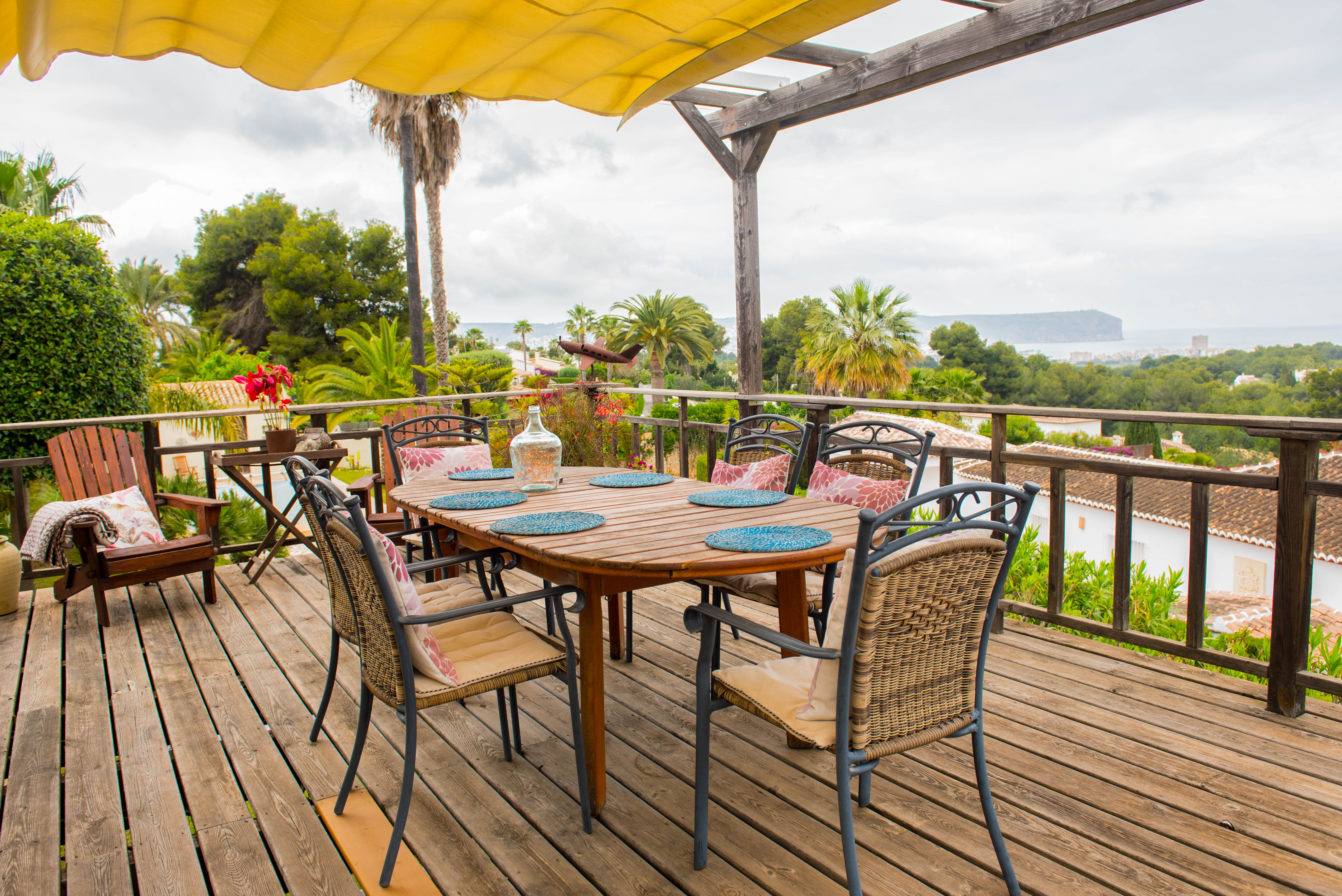 Terraza de tarima de madera con toldo extensible amarillo, equipada con zona de comedor y vistas despejadas hacia la costa y el mar.