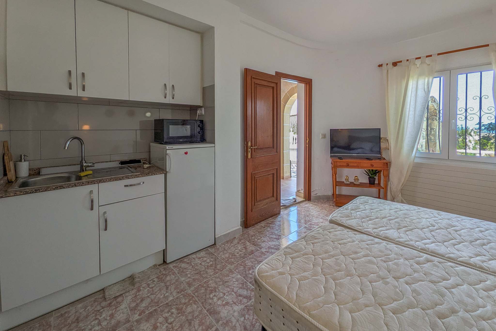 Apartamento independiente en planta baja con cocina integrada, zona de dormitorio con dos camas y acceso directo al exterior a través de una puerta de madera.