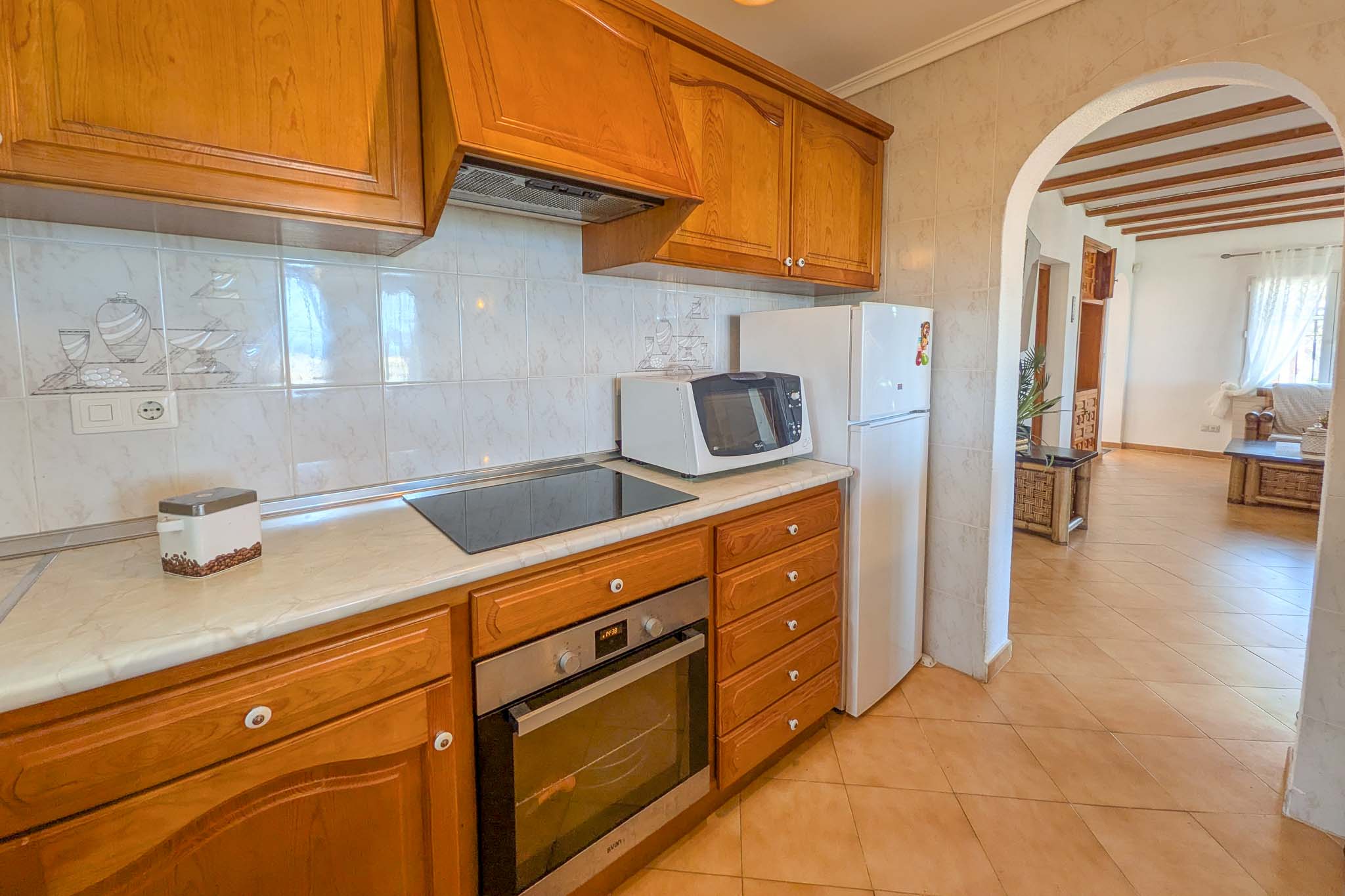 Cocina equipada con mobiliario de madera clásica, encimera de mármol y electrodomésticos integrados, conectada al salón mediante un arco tradicional.