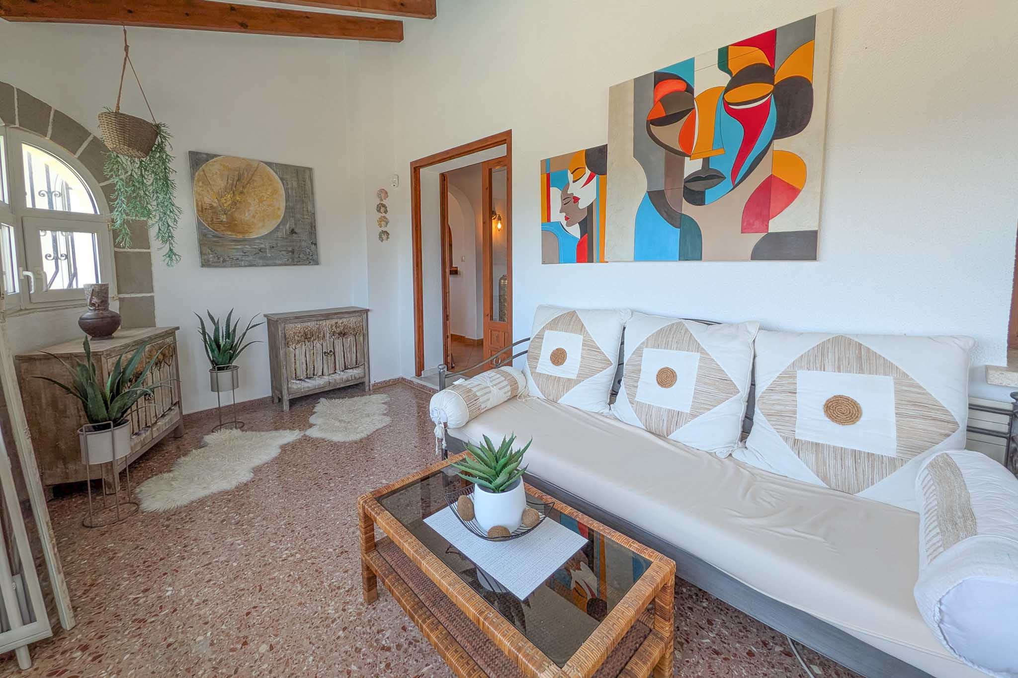 Salón luminoso con vigas de madera expuestas, suelos de terrazo y un ventanal de arco. La estancia integra mobiliario rústico con arte moderno y abundante luz natural.