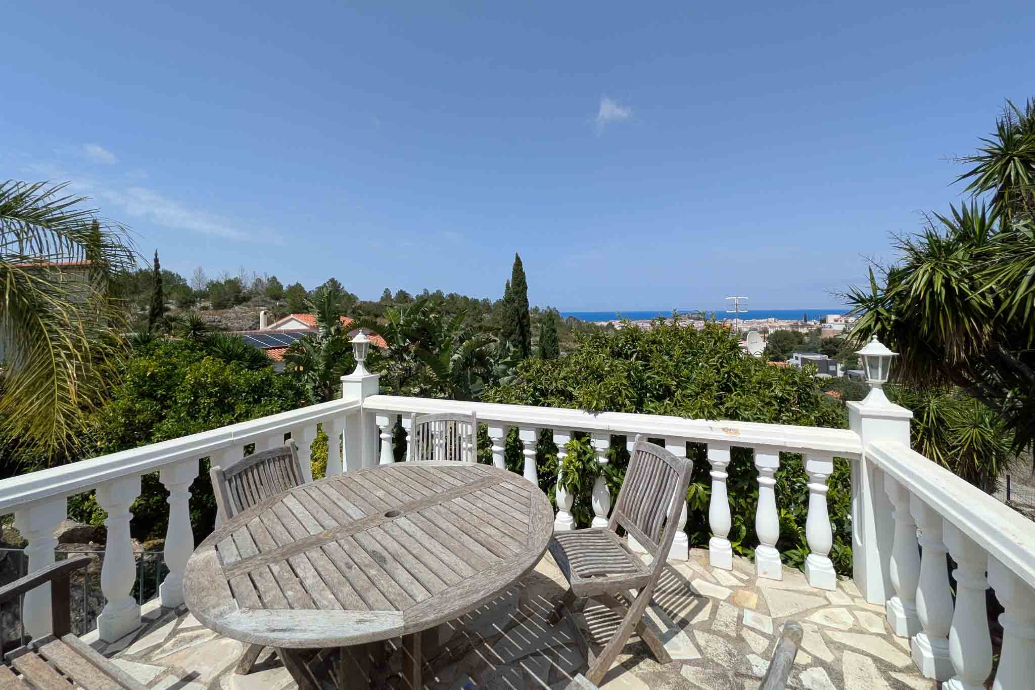 Terraza con balaustrada blanca y mobiliario de madera sobre suelo de piedra, con vistas despejadas al mar Mediterráneo y al núcleo urbano de Dénia.