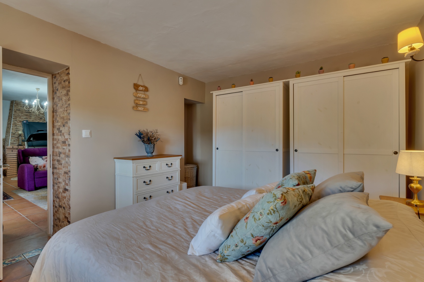 Dormitorio acogedor con amplios armarios blancos, cómoda de estilo clásico y un detalle de pared en piedra natural junto al acceso al salón.
