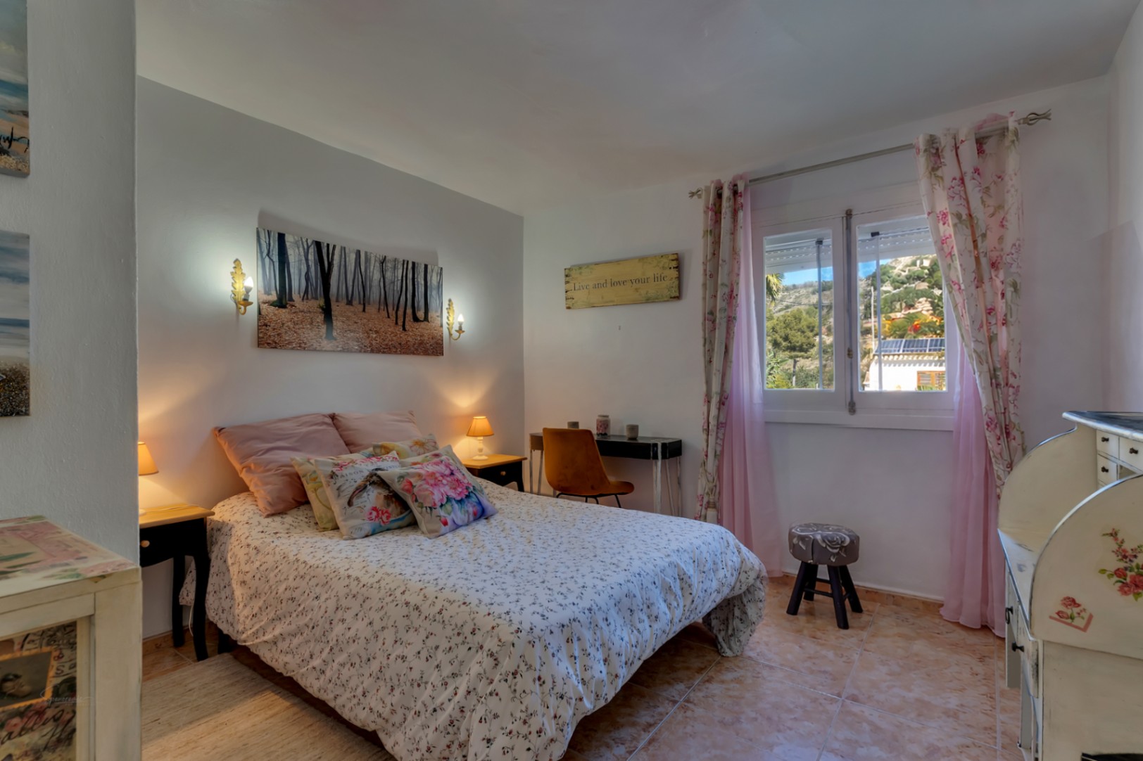 Dormitorio luminoso con suelos de gres, escritorio funcional y ventana con vistas al entorno natural de Jávea. Incluye mobiliario de estilo clásico y luz natural abundante.