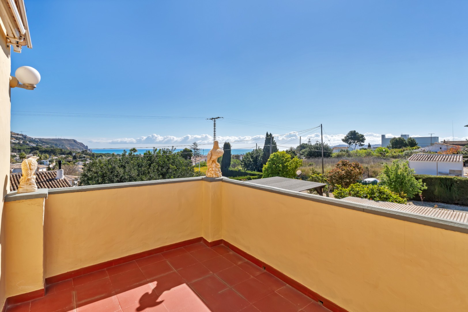 Terraza superior con suelo de baldosas de barro y muros perimetrales amarillos, ofreciendo vistas panorámicas despejadas hacia el mar Mediterráneo y la costa de Jávea.