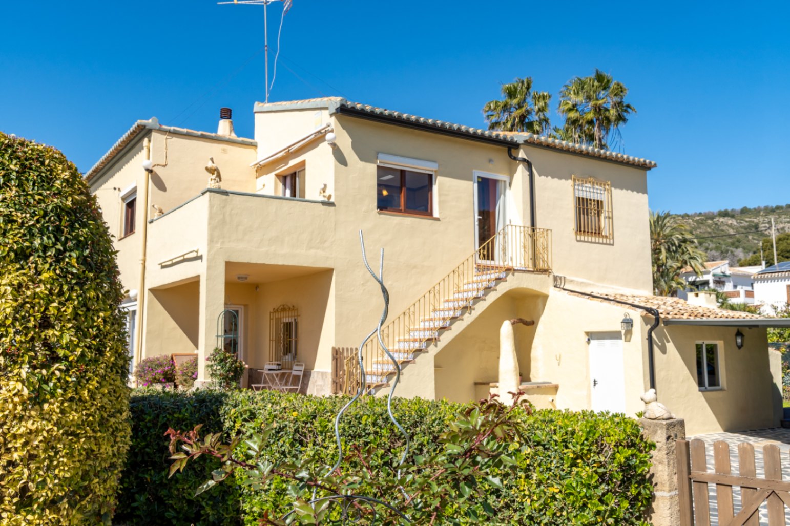 Vista exterior de la villa con fachada color crema, destacando la escalera externa con azulejos tradicionales y las amplias terrazas en ambas plantas.