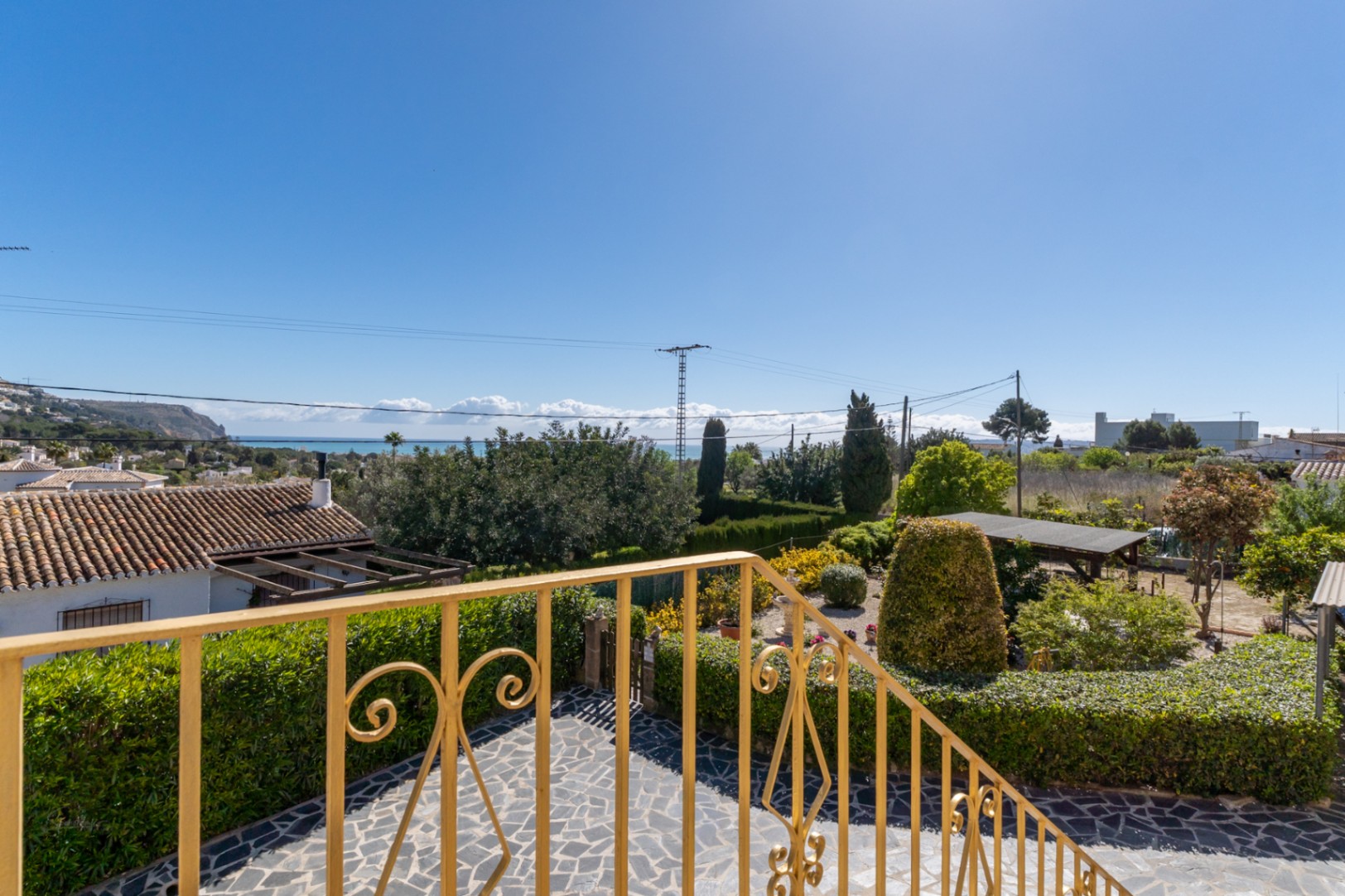 Vista panorámica al mar desde la terraza superior, con barandilla ornamental y jardín mediterráneo con pavimentos de piedra natural.
