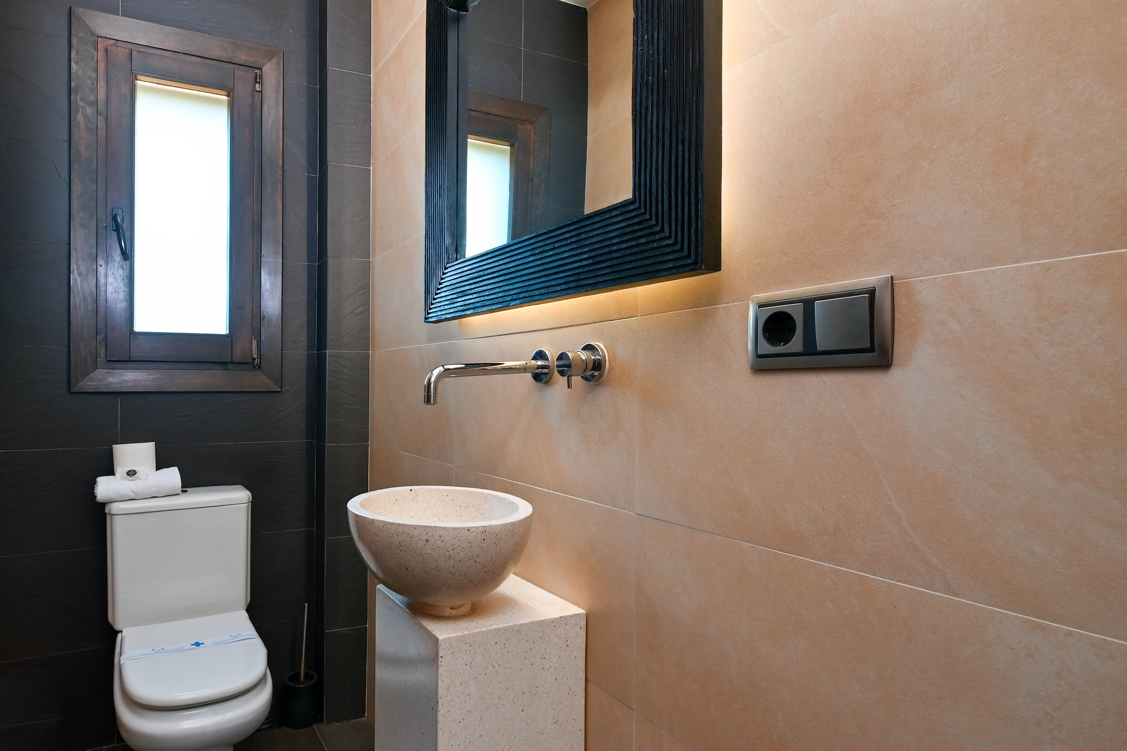 Detalle de baño con lavabo de piedra sobre pedestal y espejo con iluminación integrada.