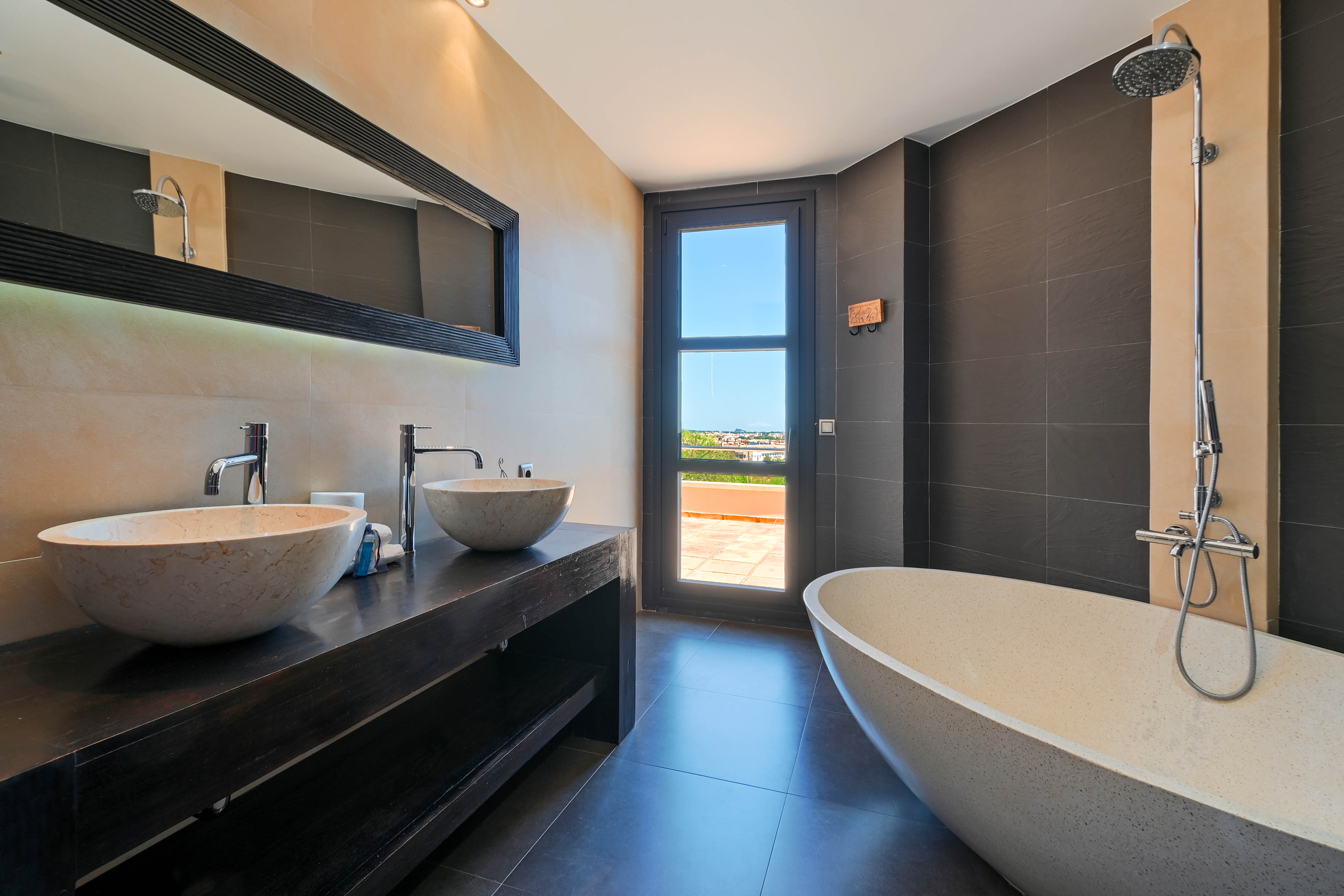 Elegante baño con lavabo doble de piedra y bañera exenta, con acceso a terraza exterior.