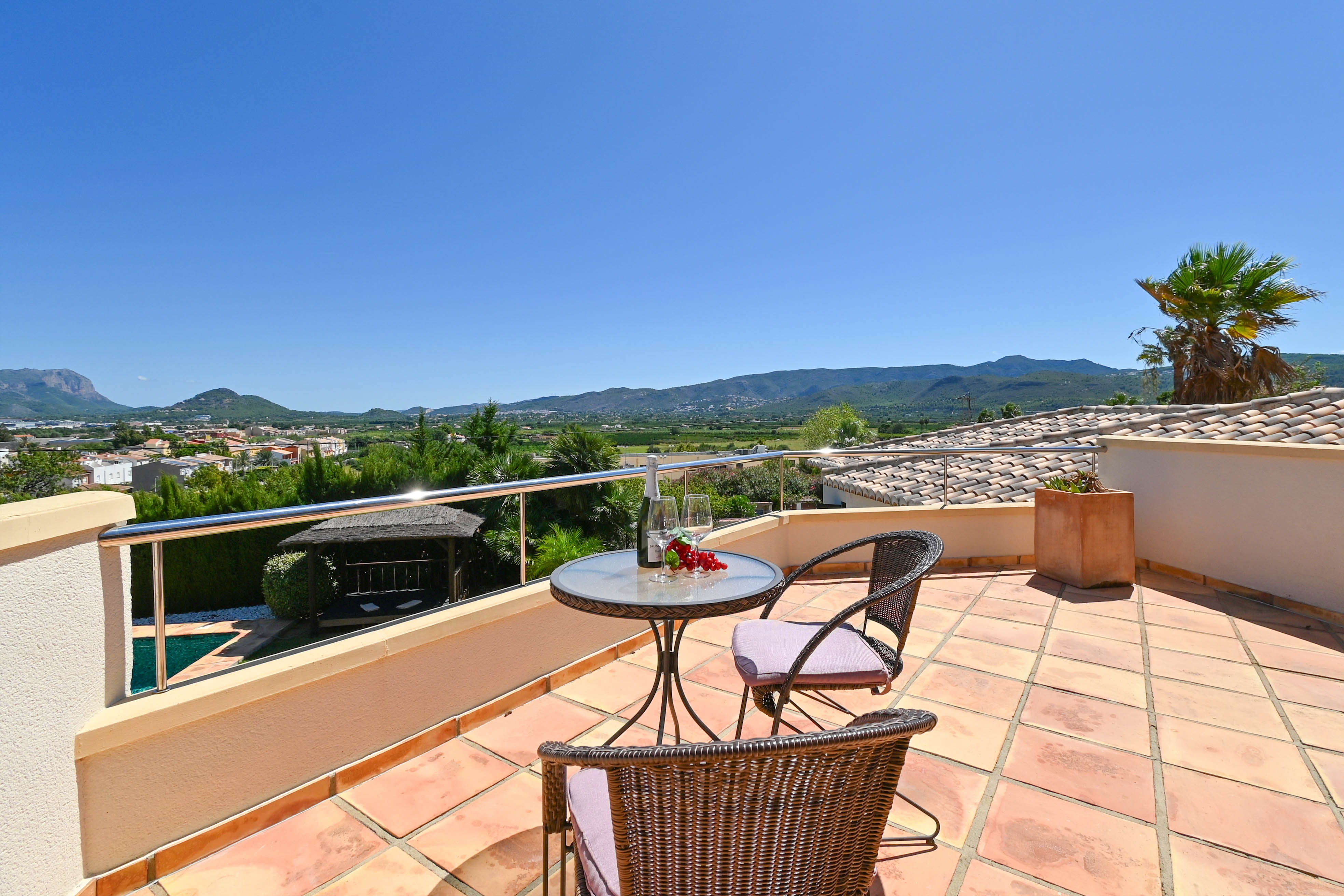 Terraza con mesa de cristal, sillas de mimbre y vistas al valle y la montaña.