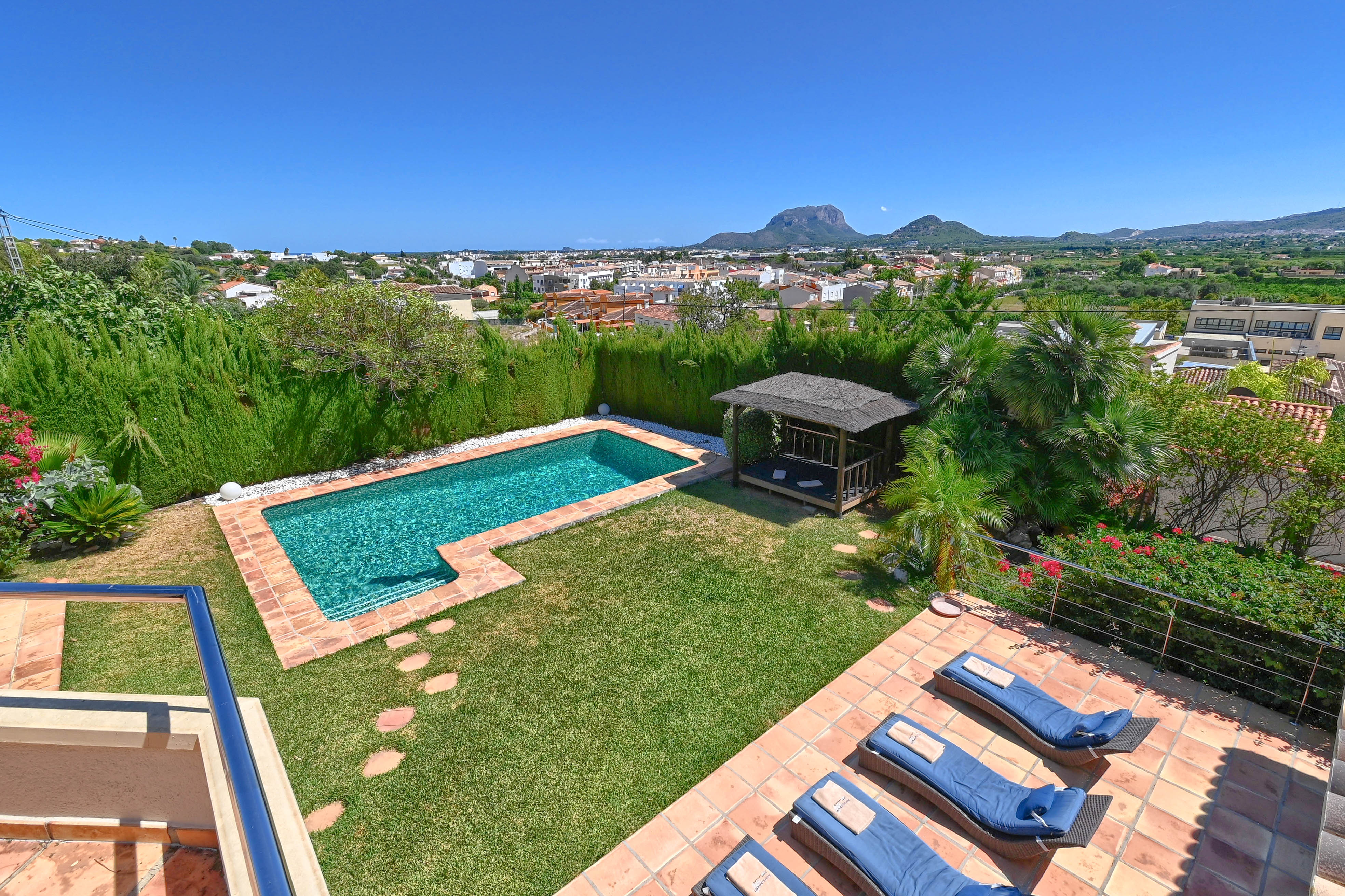 Vista elevada del jardín con piscina turquesa y cenador de paja.