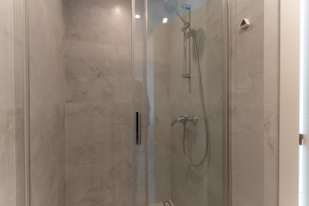Detalle de la ducha con mampara de cristal y revestimiento cerámico imitación mármol.
