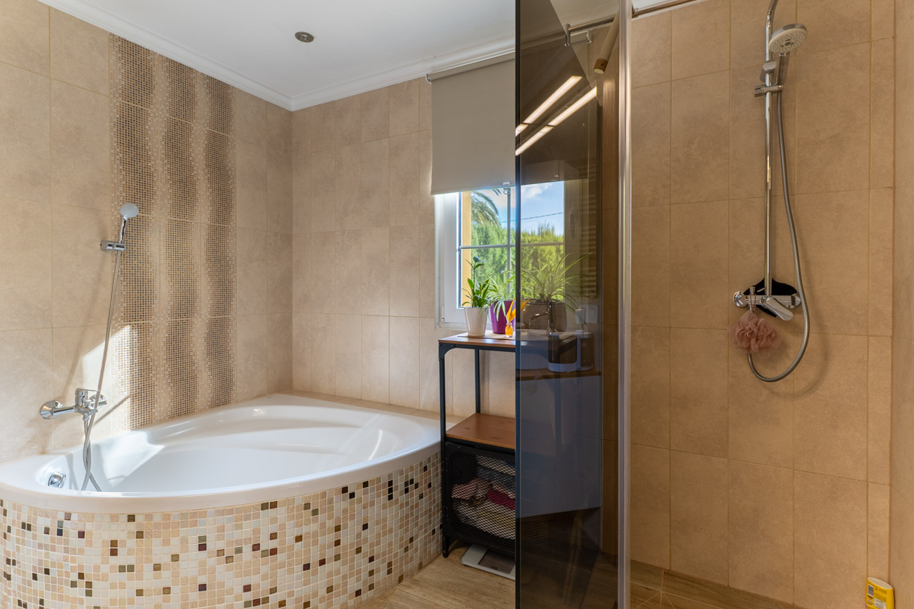 Detalle del baño con bañera esquinera de mosaico y ducha con mampara de cristal.