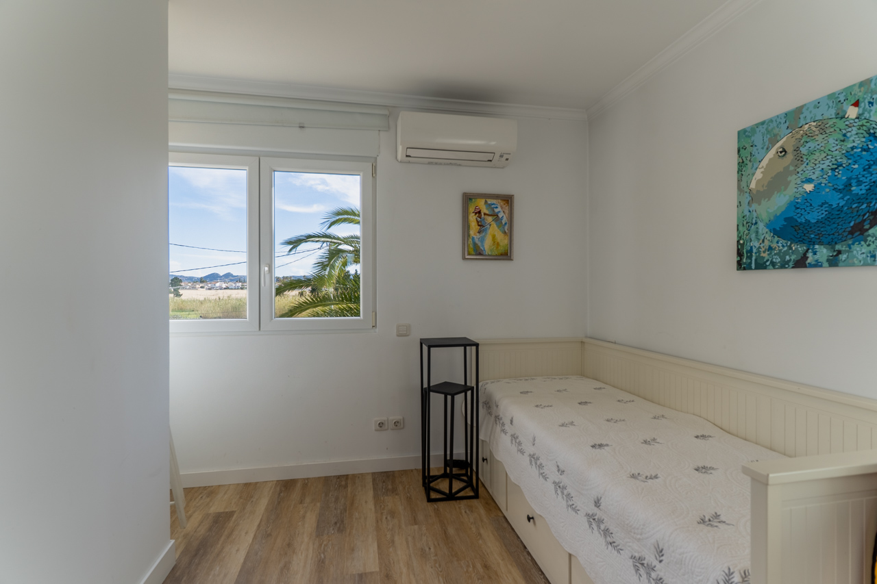 Habitación luminosa con cama individual, decoración moderna y vistas al exterior con palmeras.