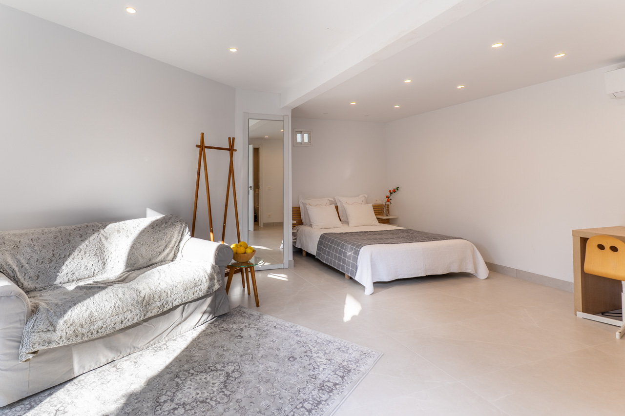Luminoso dormitorio con sofá, cama doble y escritorio, iluminado con focos empotrados.