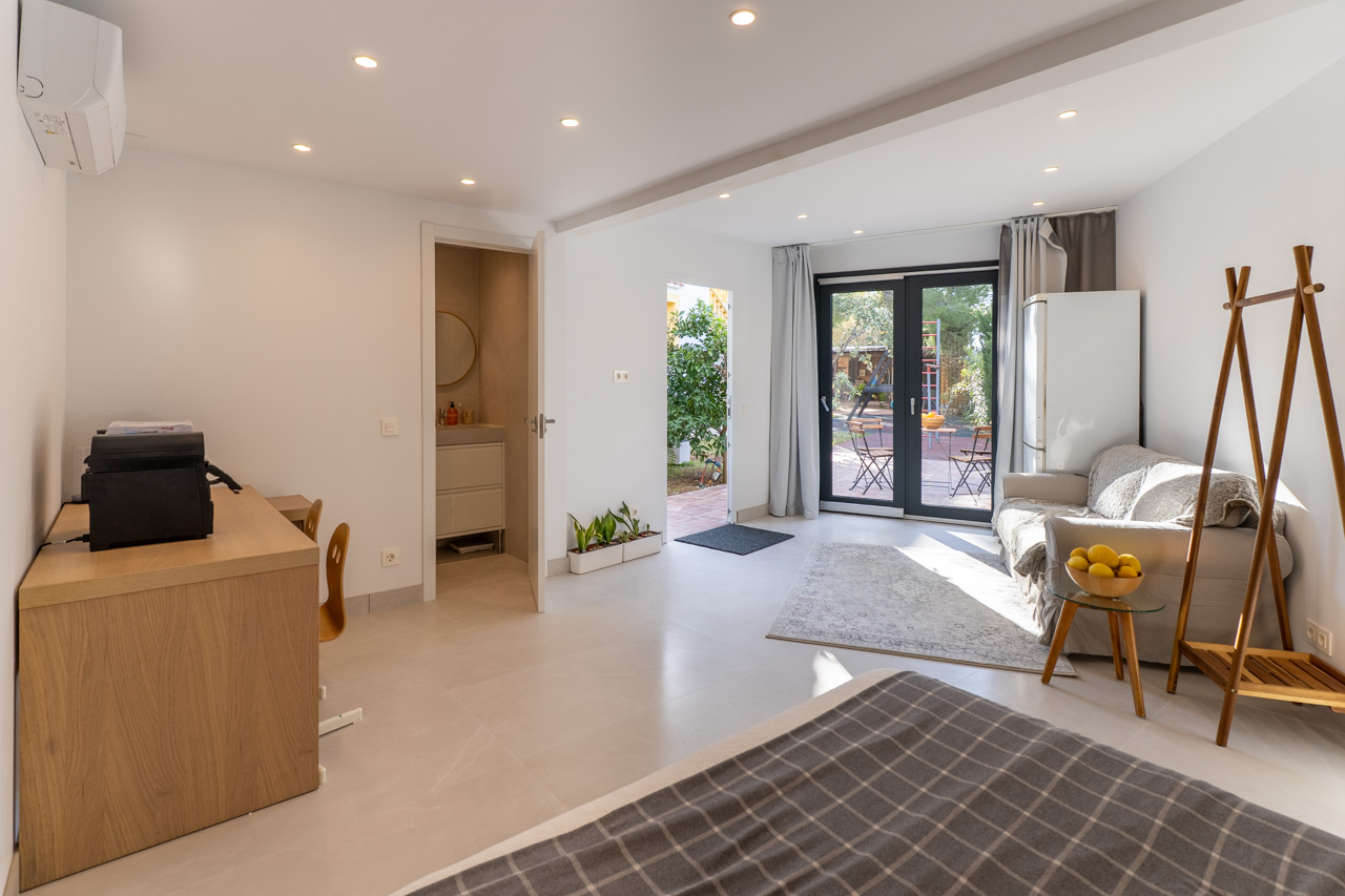 Luminoso espacio multifuncional con acceso al jardín, baño en-suite y mobiliario funcional en tonos neutros.