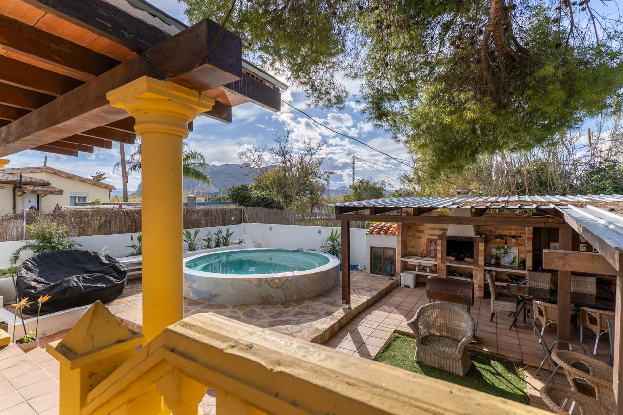 Vista de la zona de piscina con barbacoa techada, desde la terraza con barandilla amarilla.