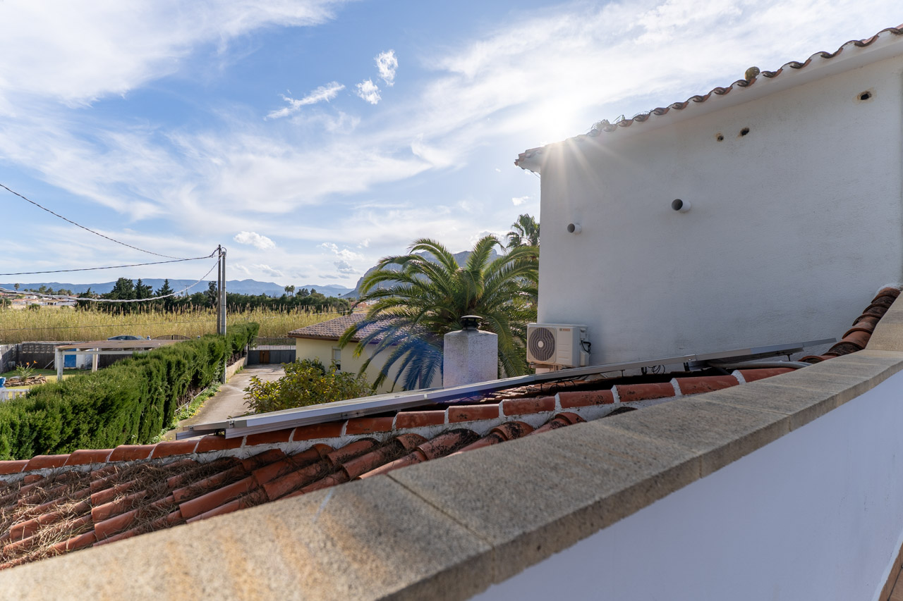 Vista desde la azotea con tejas de arcilla y panel solar. Al fondo, vegetación y montañas.