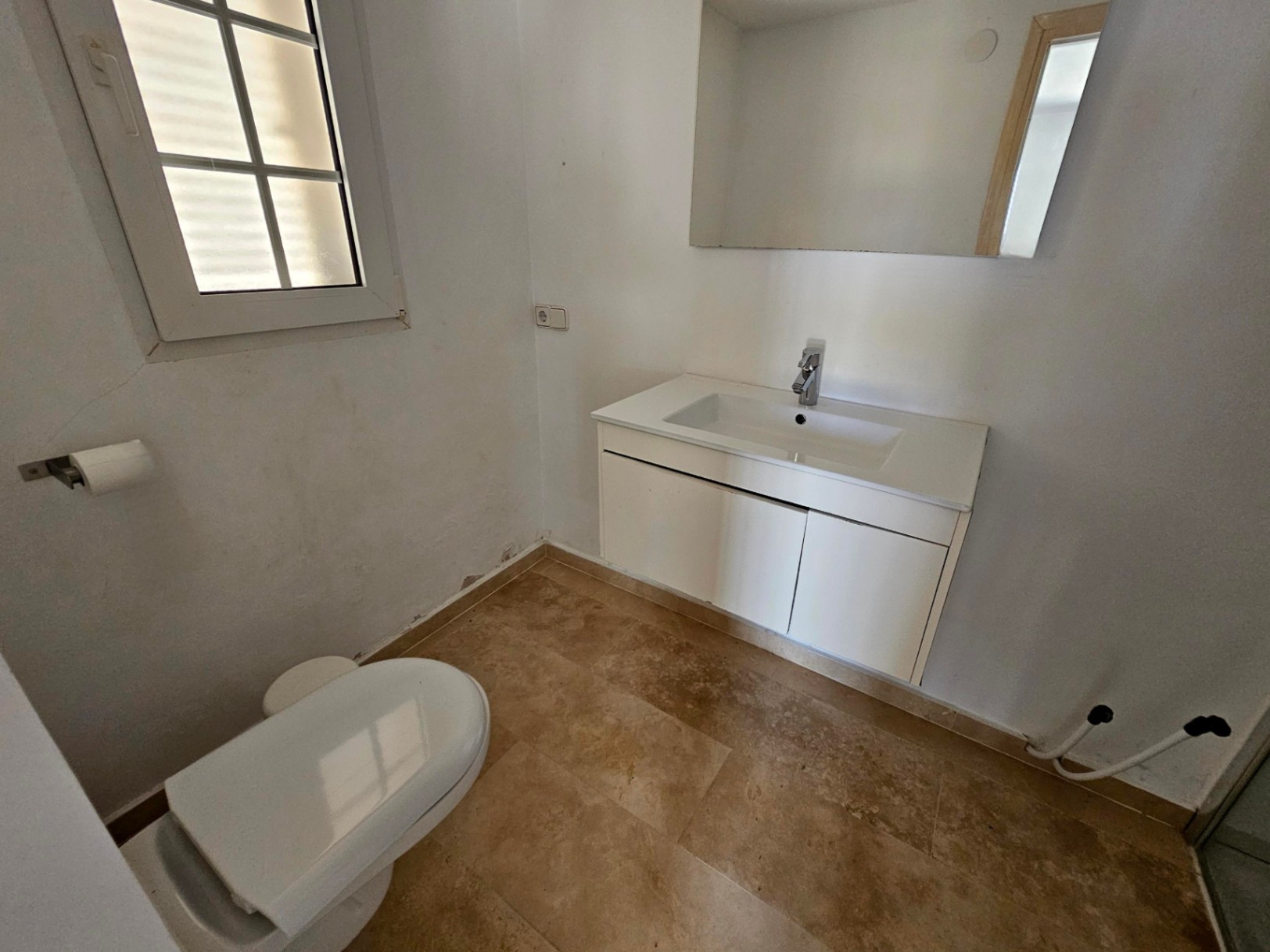 Aseo con lavabo moderno y suelo de baldosas color crema.