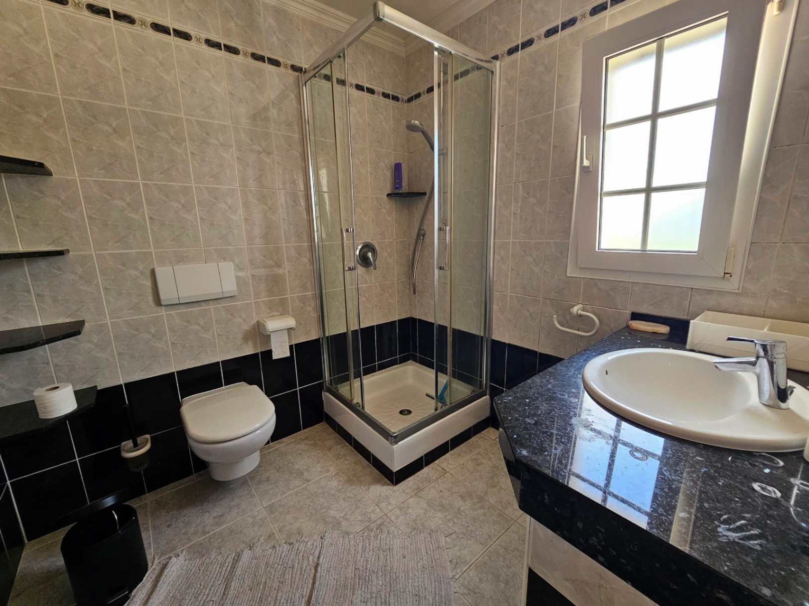 Cuarto de baño con ducha esquinera y encimera de granito negro.