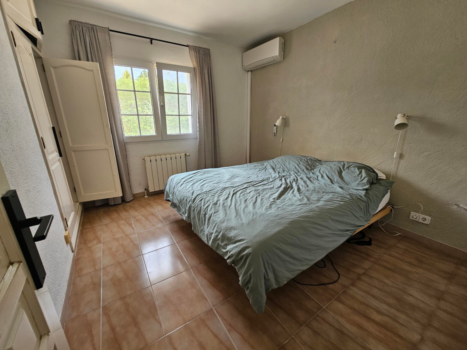 Dormitorio con cama doble, armario blanco y suelo de baldosas color terracota.