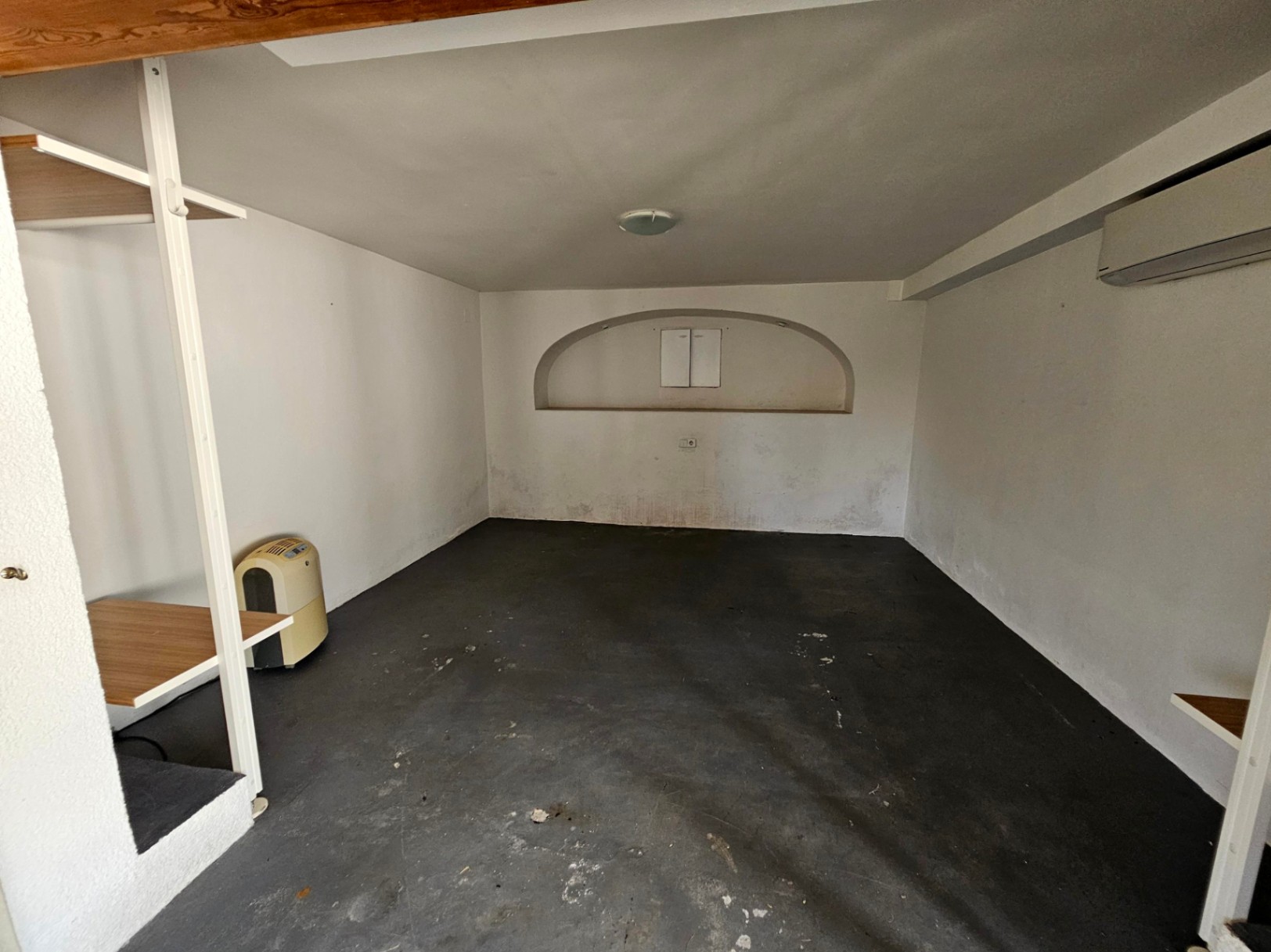 Espacio interior con suelo oscuro, paredes blancas y nicho decorativo con estantes.