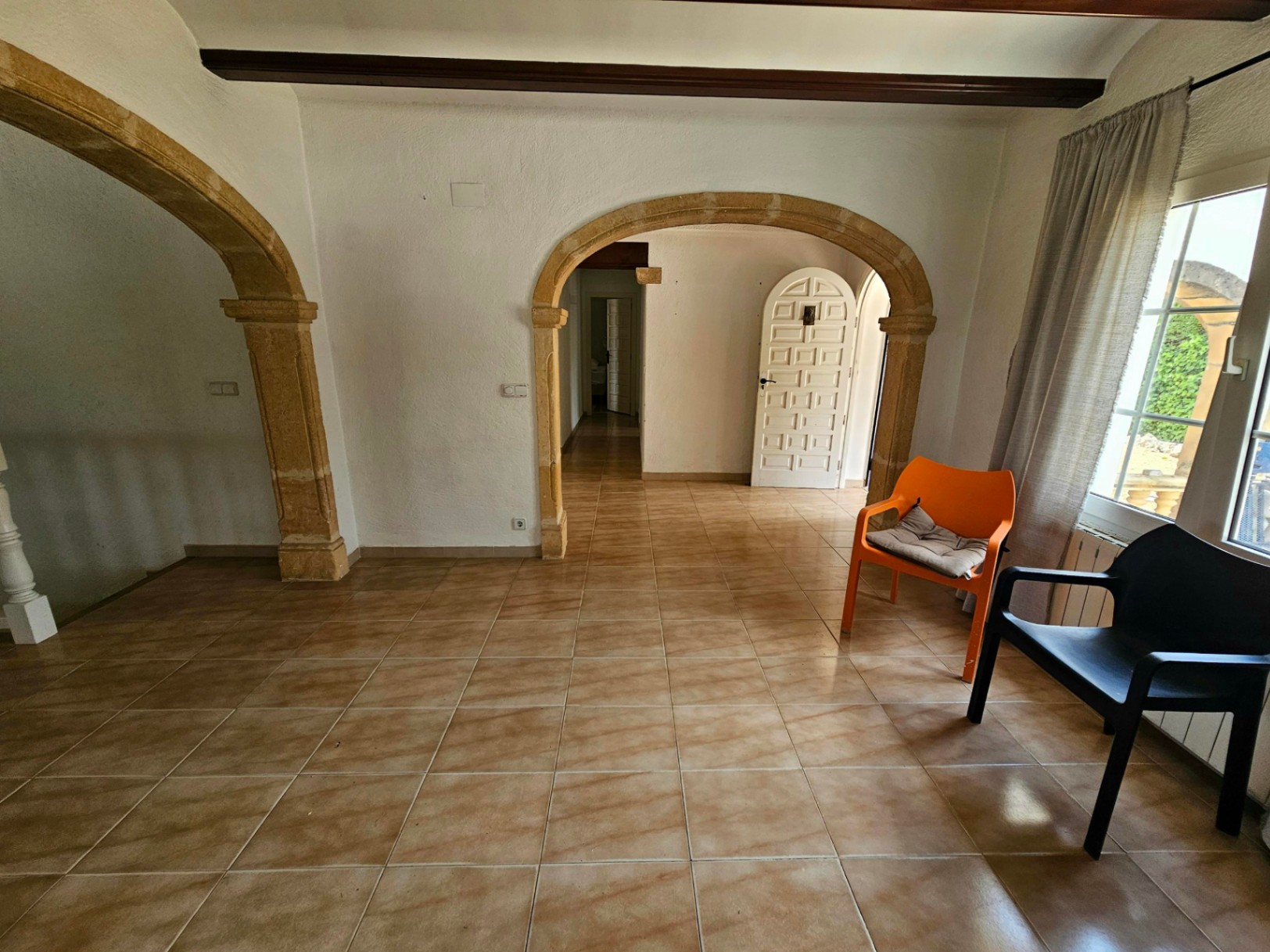 Salón con arcos de piedra arenisca, suelo de baldosas color crema y sillas de diseño.