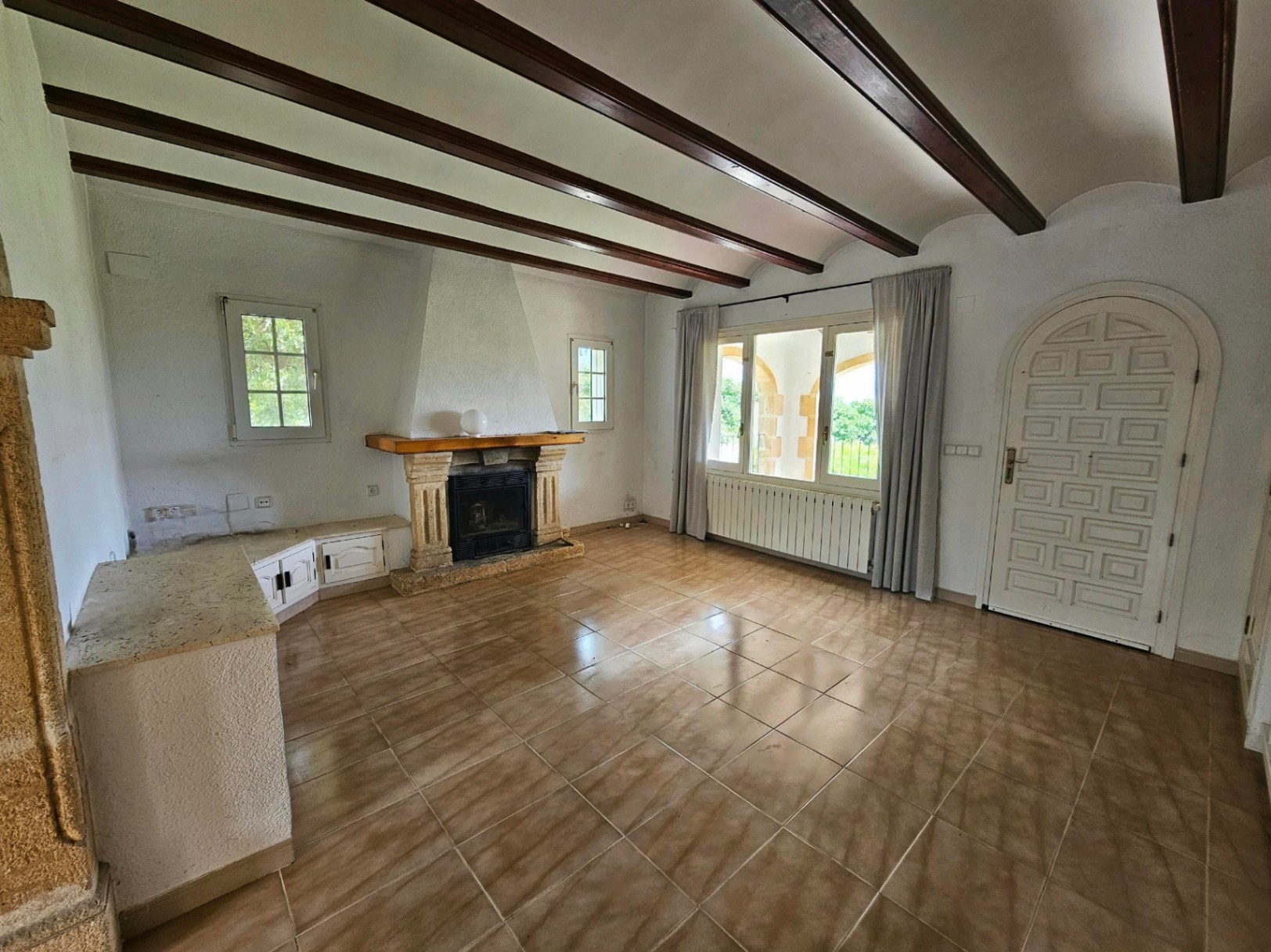 Salón con chimenea de piedra, vigas de madera y suelo de baldosas.
