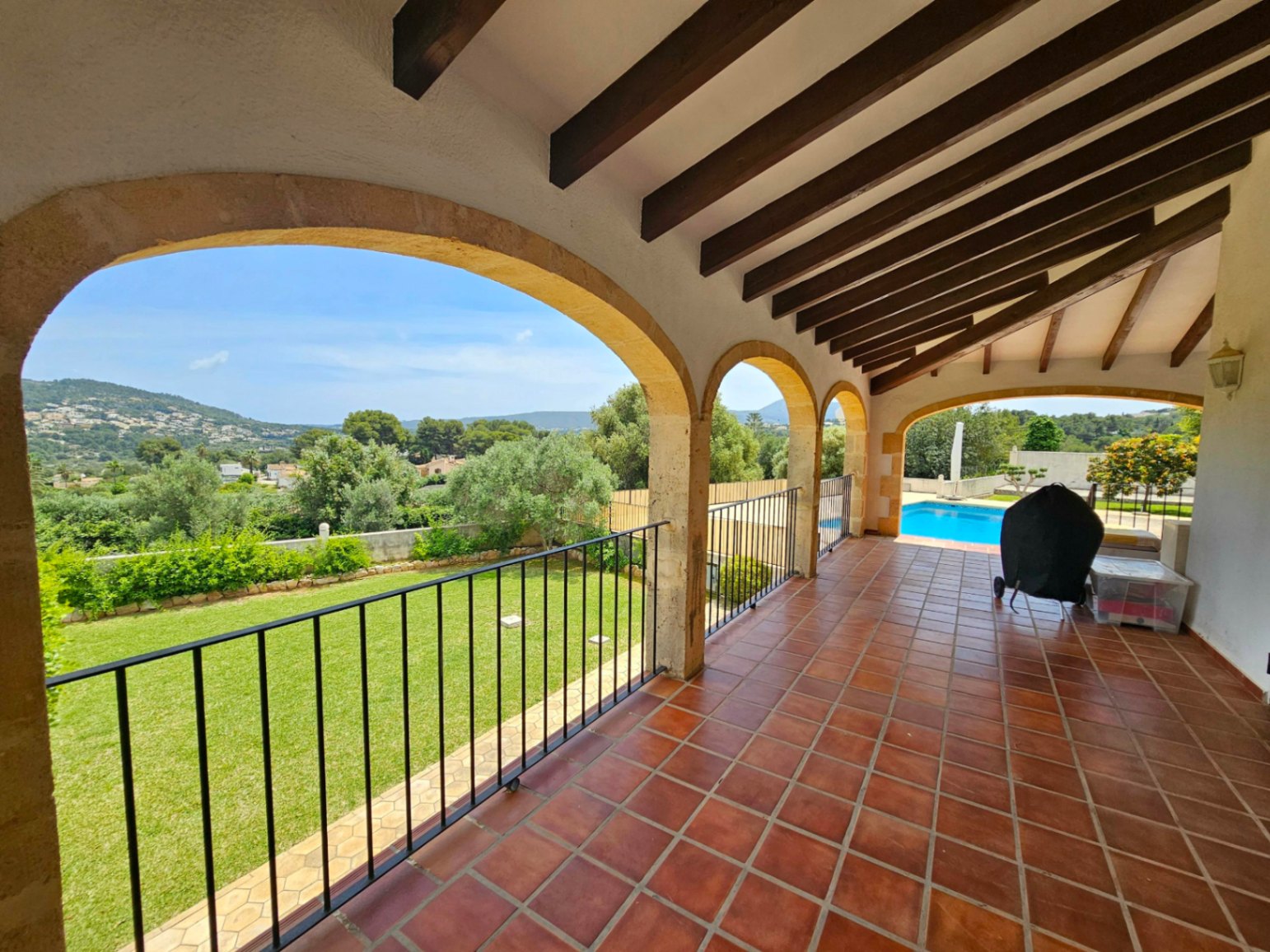 Terraza cubierta con arcos de piedra y vistas al jardín y piscina.