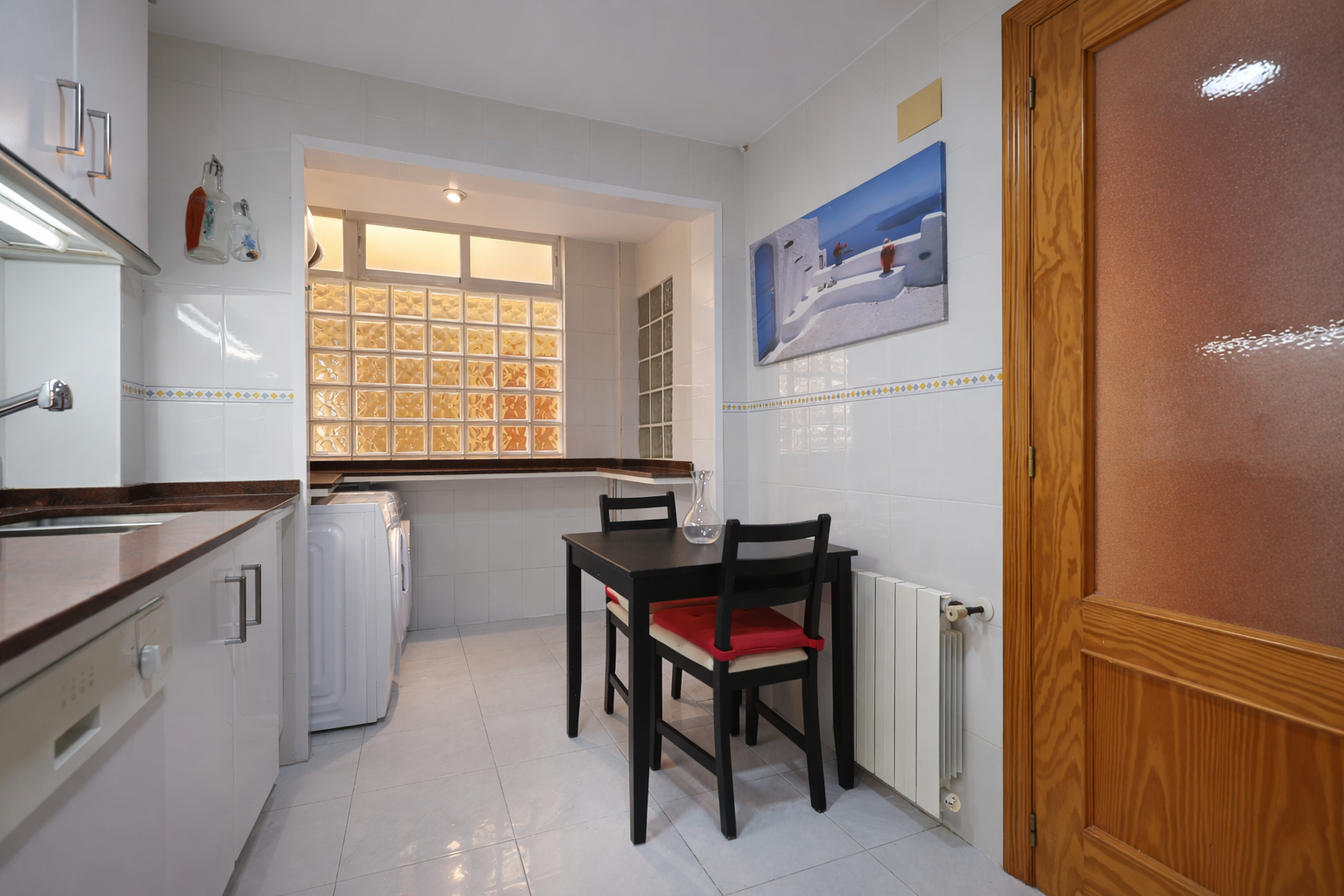 Cocina funcional con mesa de comedor, electrodomésticos blancos y ventana de bloques de vidrio.