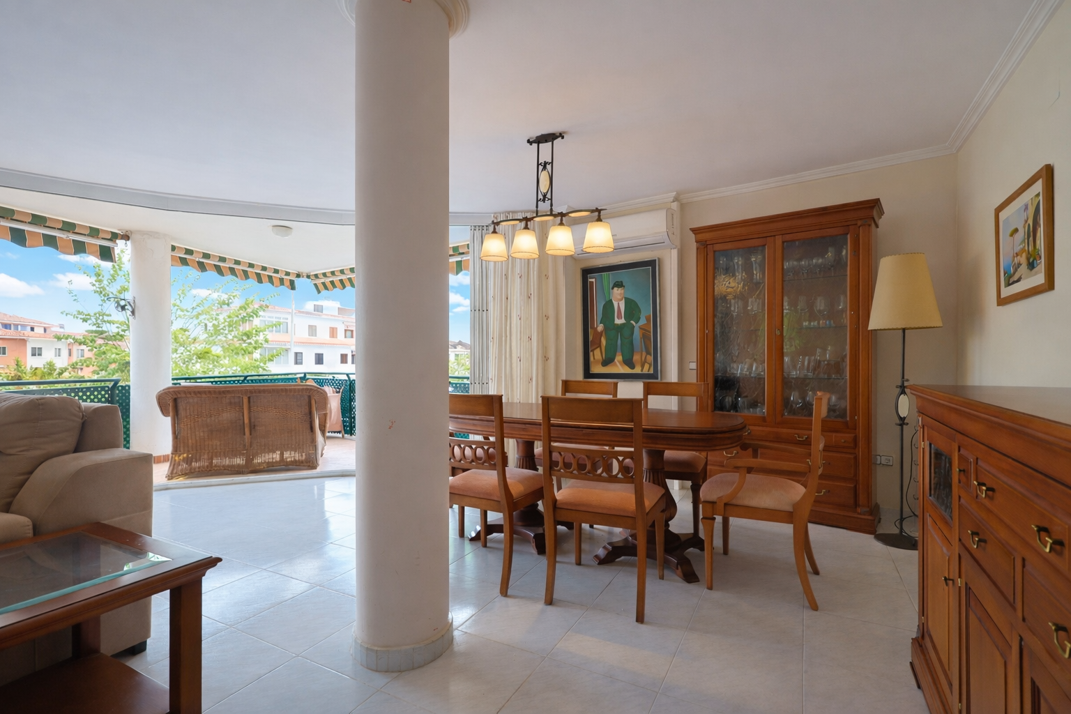 Comedor luminoso con acceso a terraza, destacando mesa de madera y vitrina clásica.
