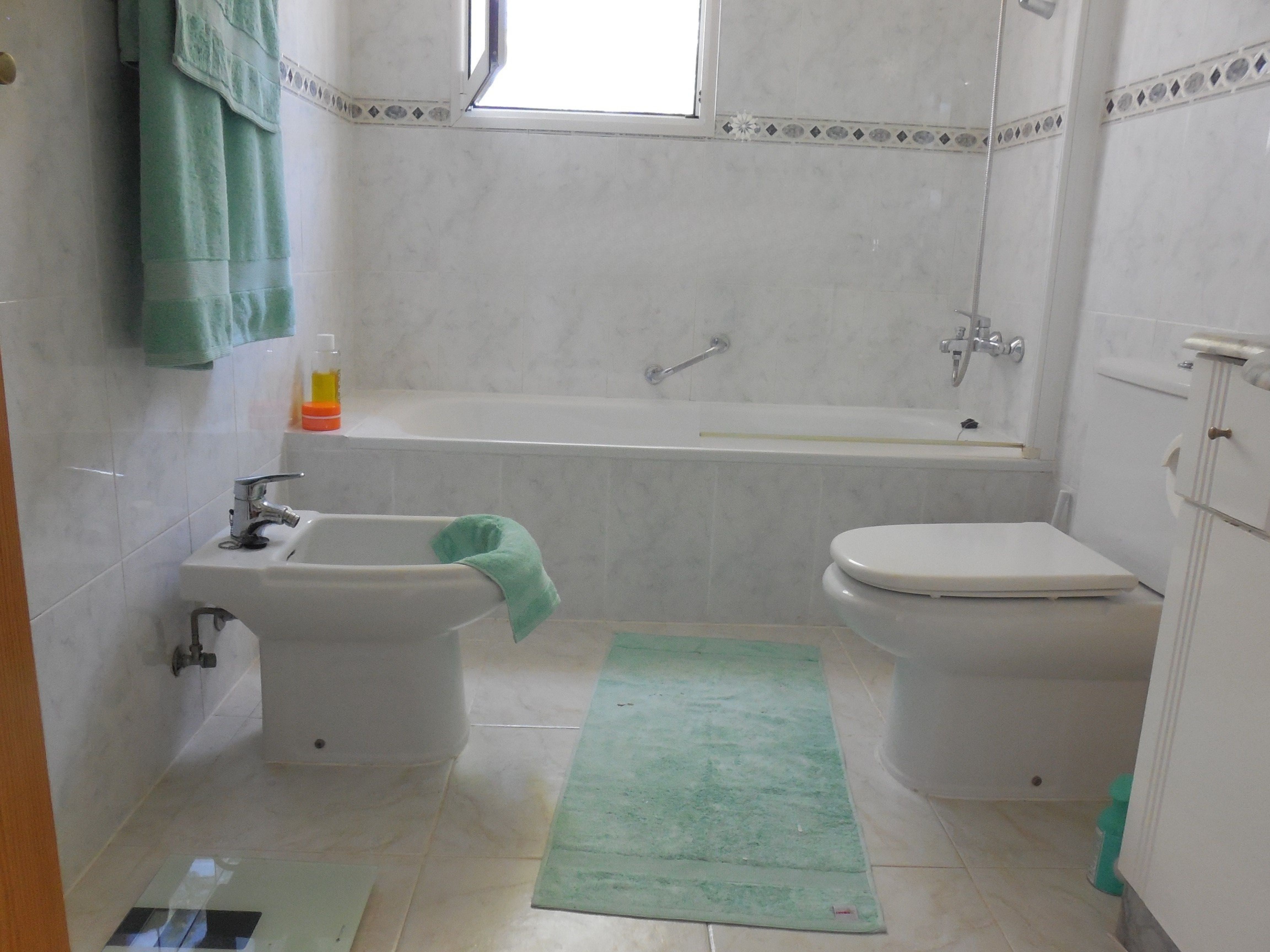 Cuarto de baño con azulejos de mármol, bañera, bidé y toallas verde menta.
