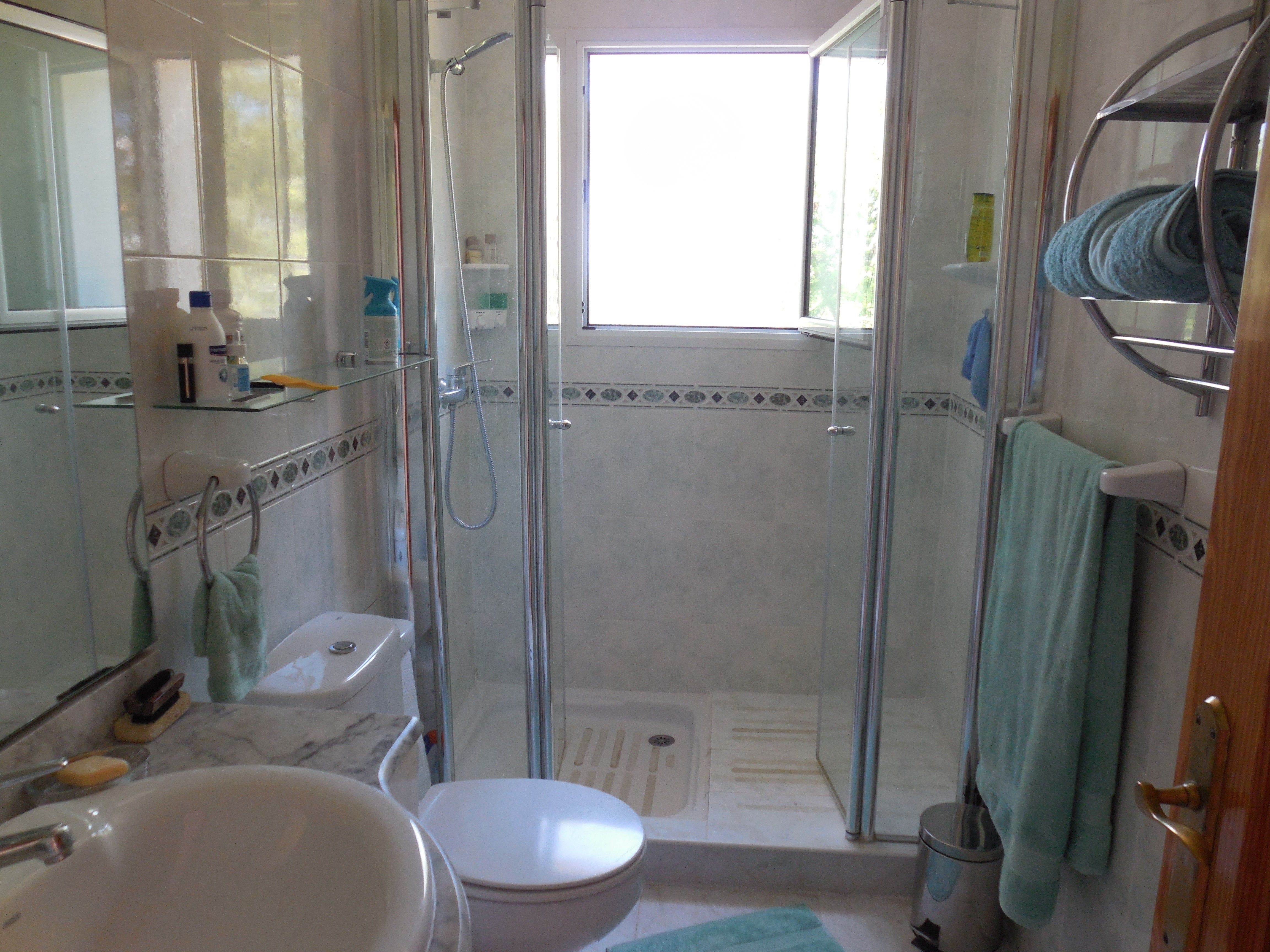 Cuarto de baño con ducha de mampara, lavabo de mármol y azulejos decorativos.