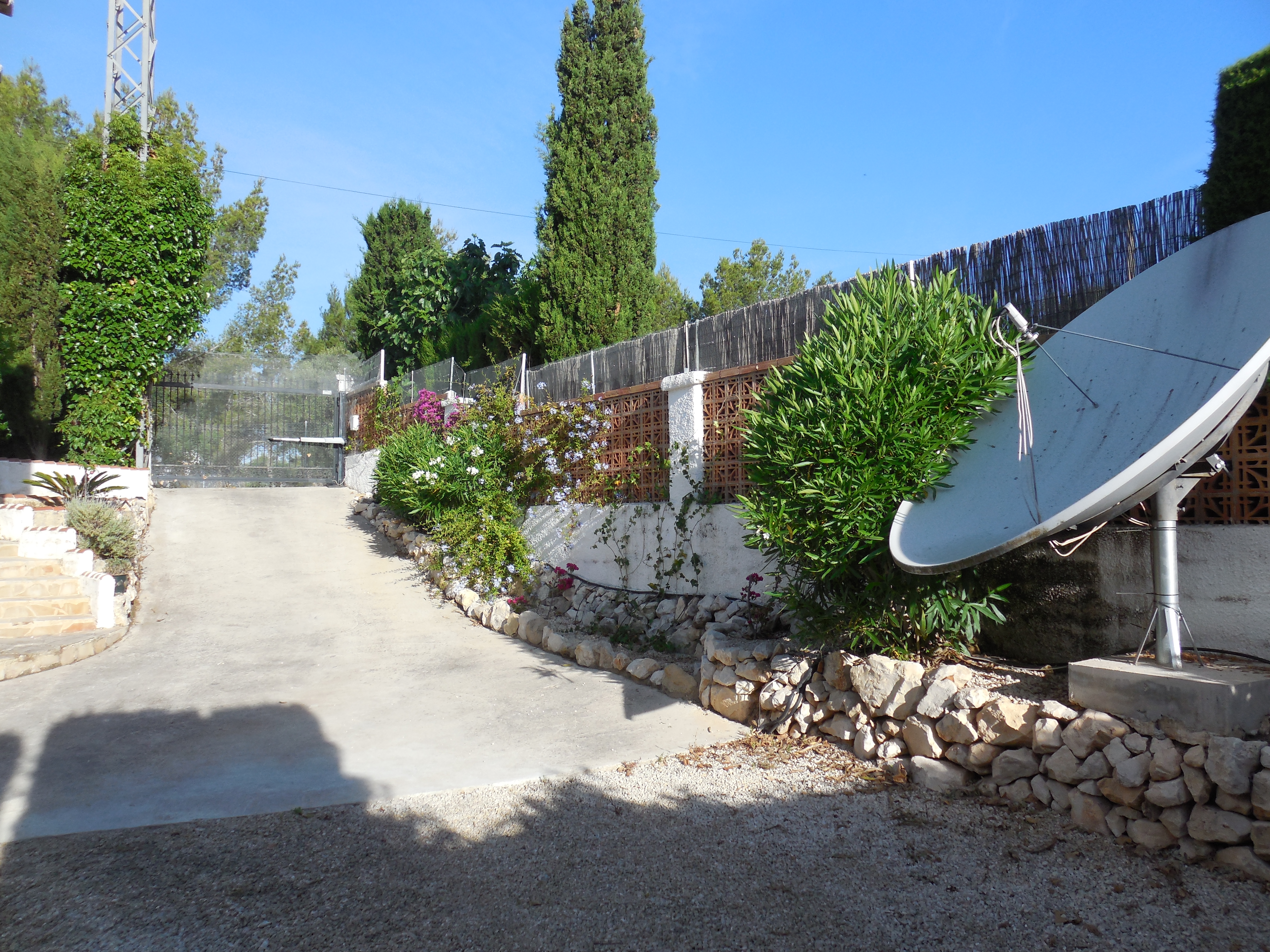 Entrada a la propiedad con camino de cemento, valla de ladrillo y vegetación.