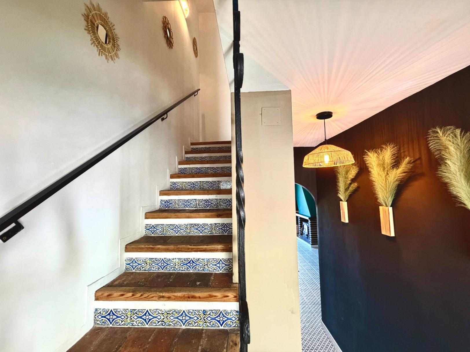 Detalle de escalera con azulejos decorativos y pared con espejos y apliques de diseño.