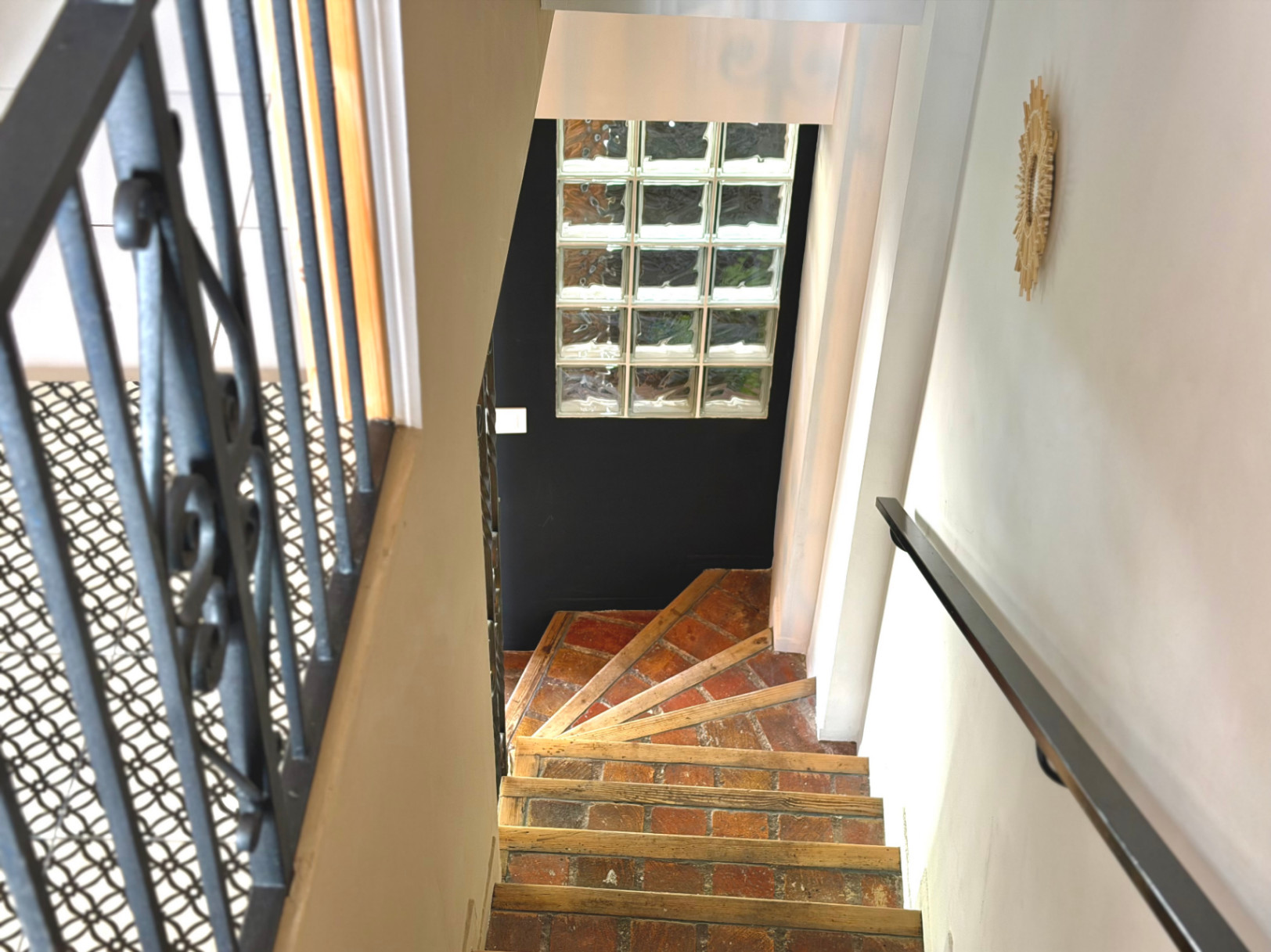 Detalle de escalera interior con barandilla de hierro forjado y escalones de ladrillo visto.