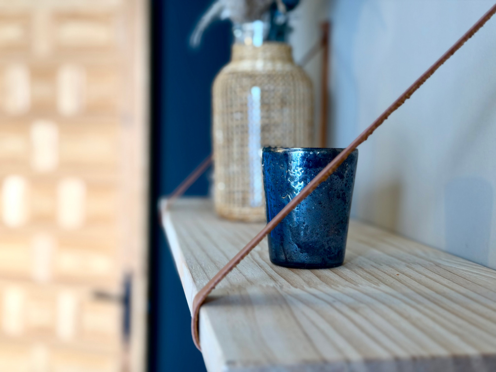 Detalle de estante de madera clara con decoración: vaso azul texturizado y botella de vidrio con funda de mimbre.