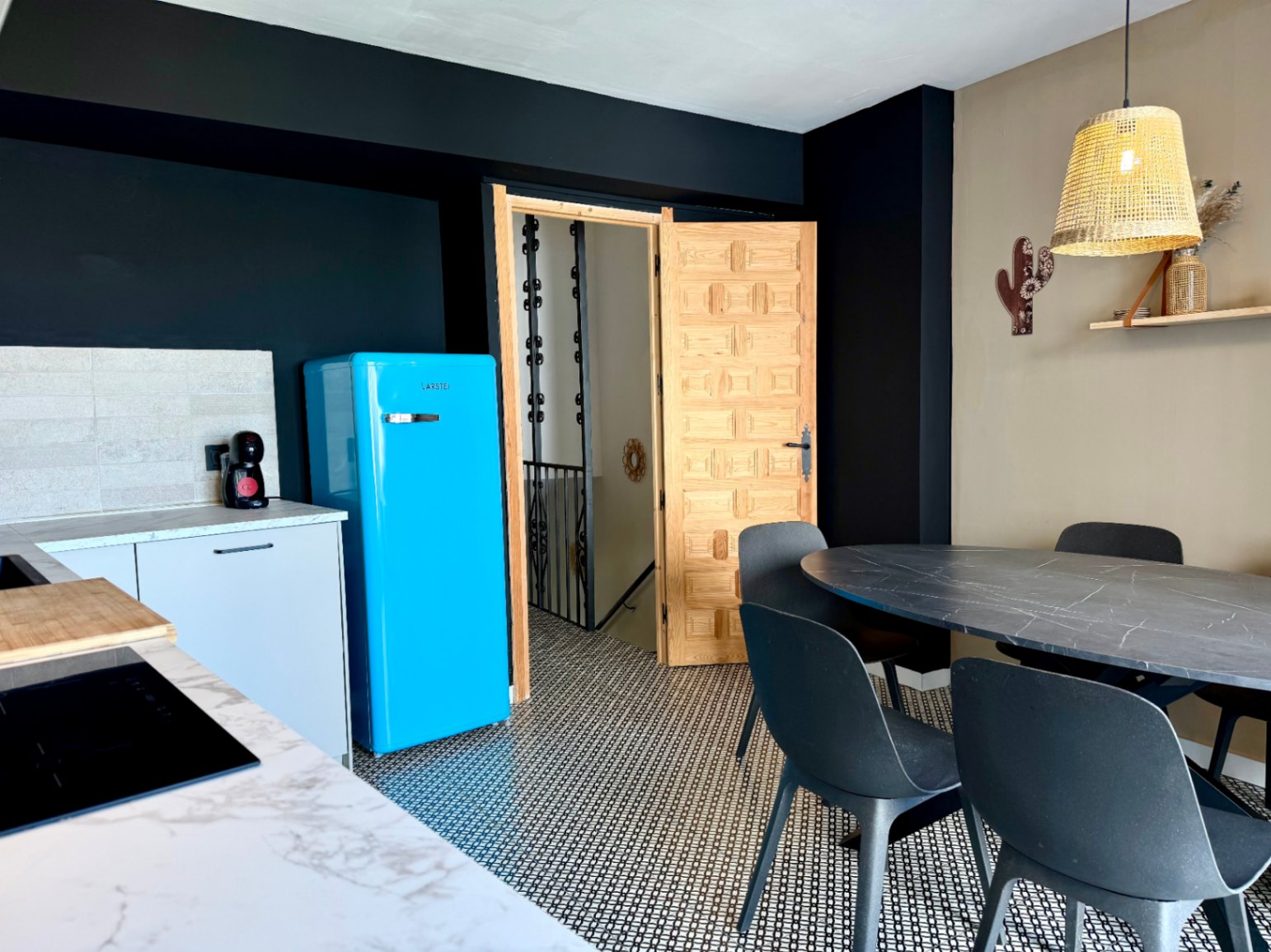 Detalle de la cocina con nevera azul retro, mesa de comedor ovalada y puerta de madera tallada.