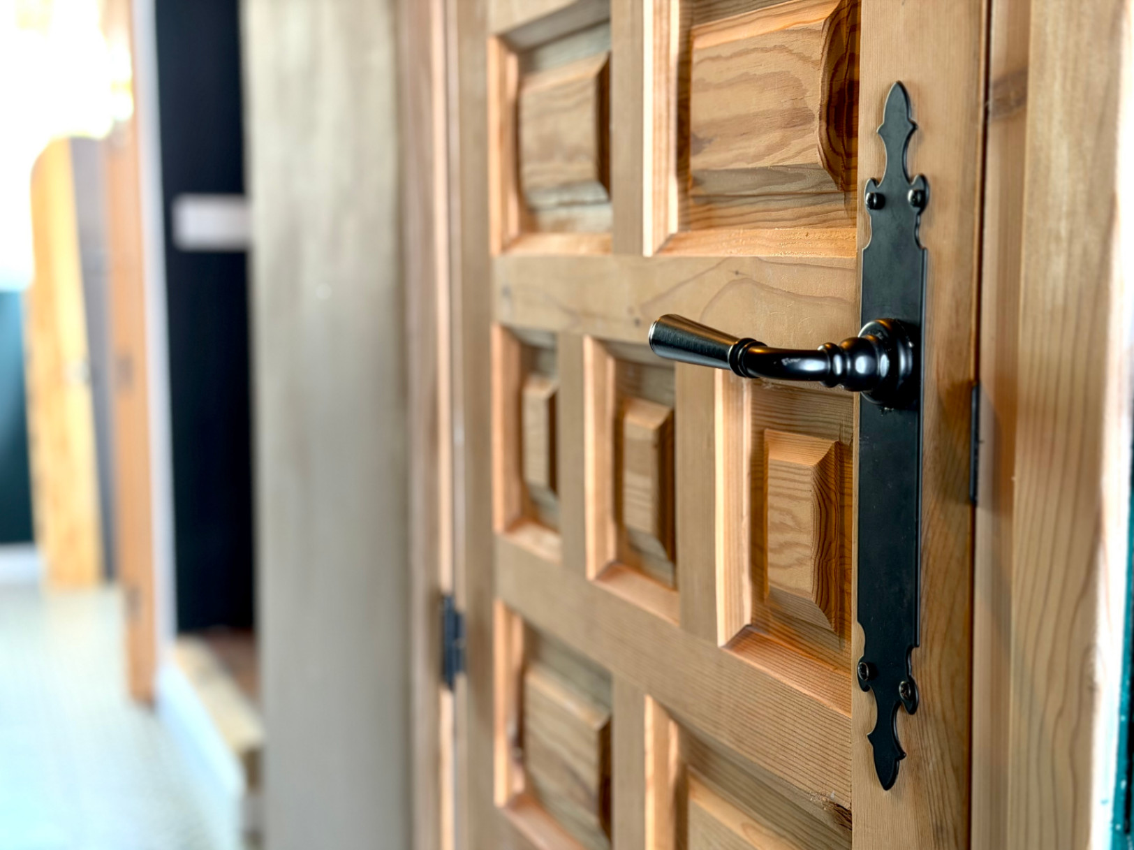 Detalle de puerta de madera con diseño en relieve y herraje negro forjado.