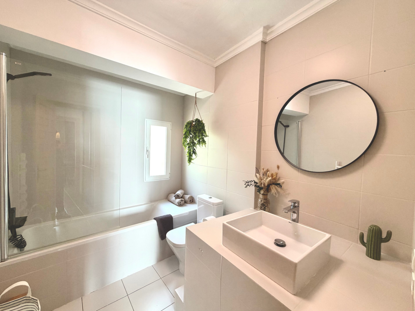 Detalle del baño renovado con bañera, lavabo moderno, espejo circular y toques decorativos.