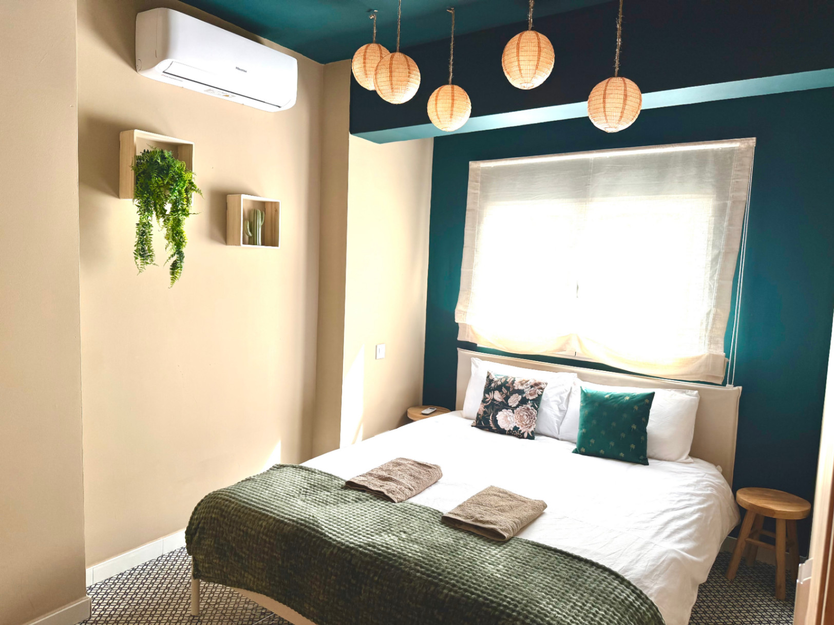 Dormitorio con paredes color crema y detalles en verde azulado. Iluminación colgante y decoración minimalista.