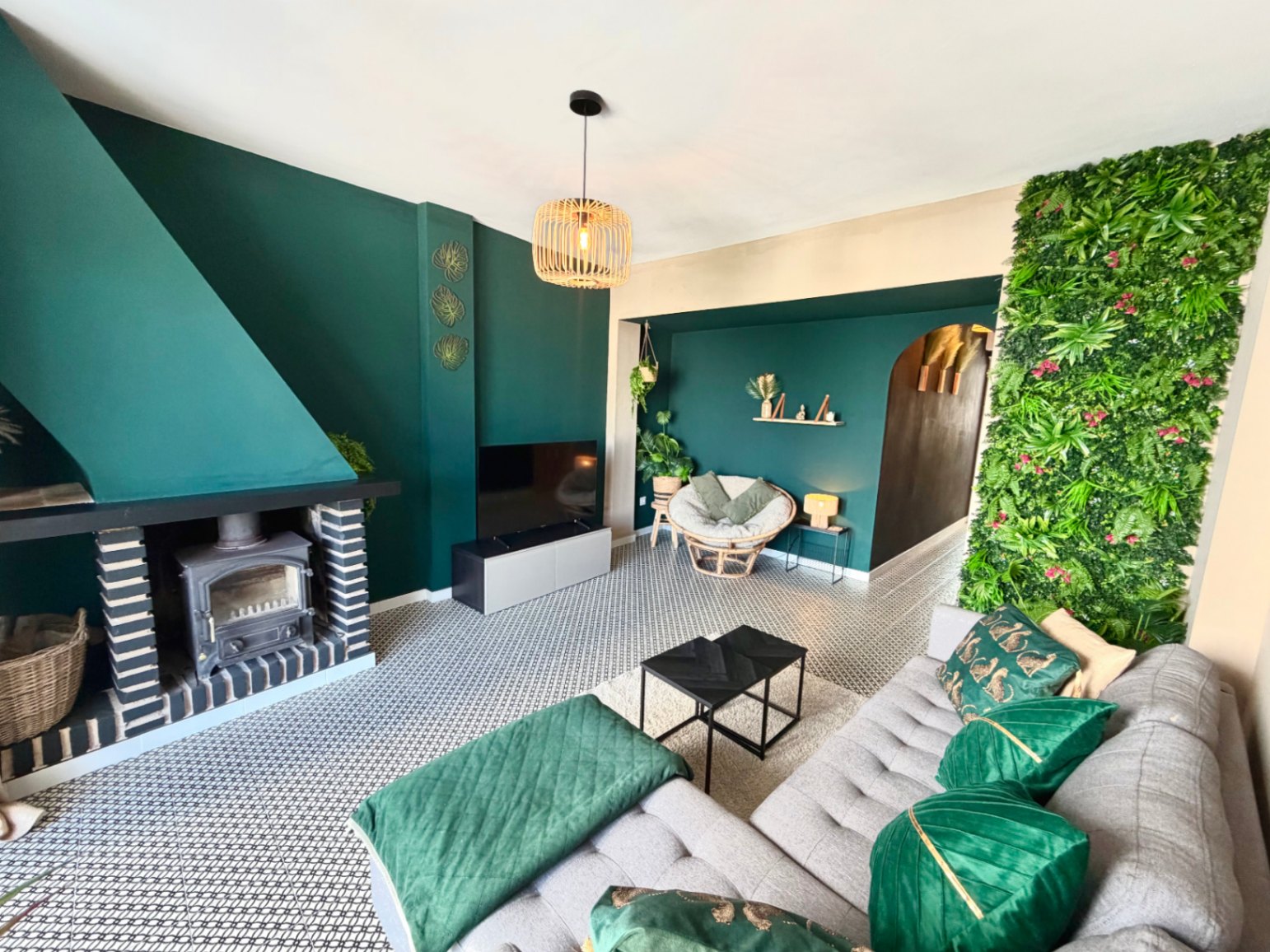 Salón con chimenea rústica, pared verde y suelo geométrico. Iluminación colgante de mimbre.