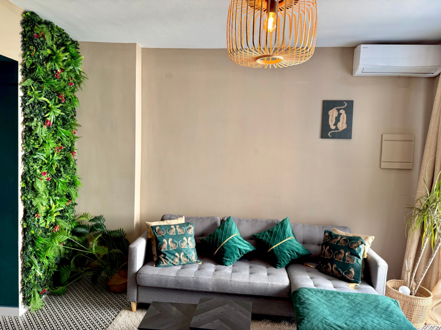 Salón luminoso con pared verde vertical, sofá gris con cojines decorativos y mesa de centro oscura.