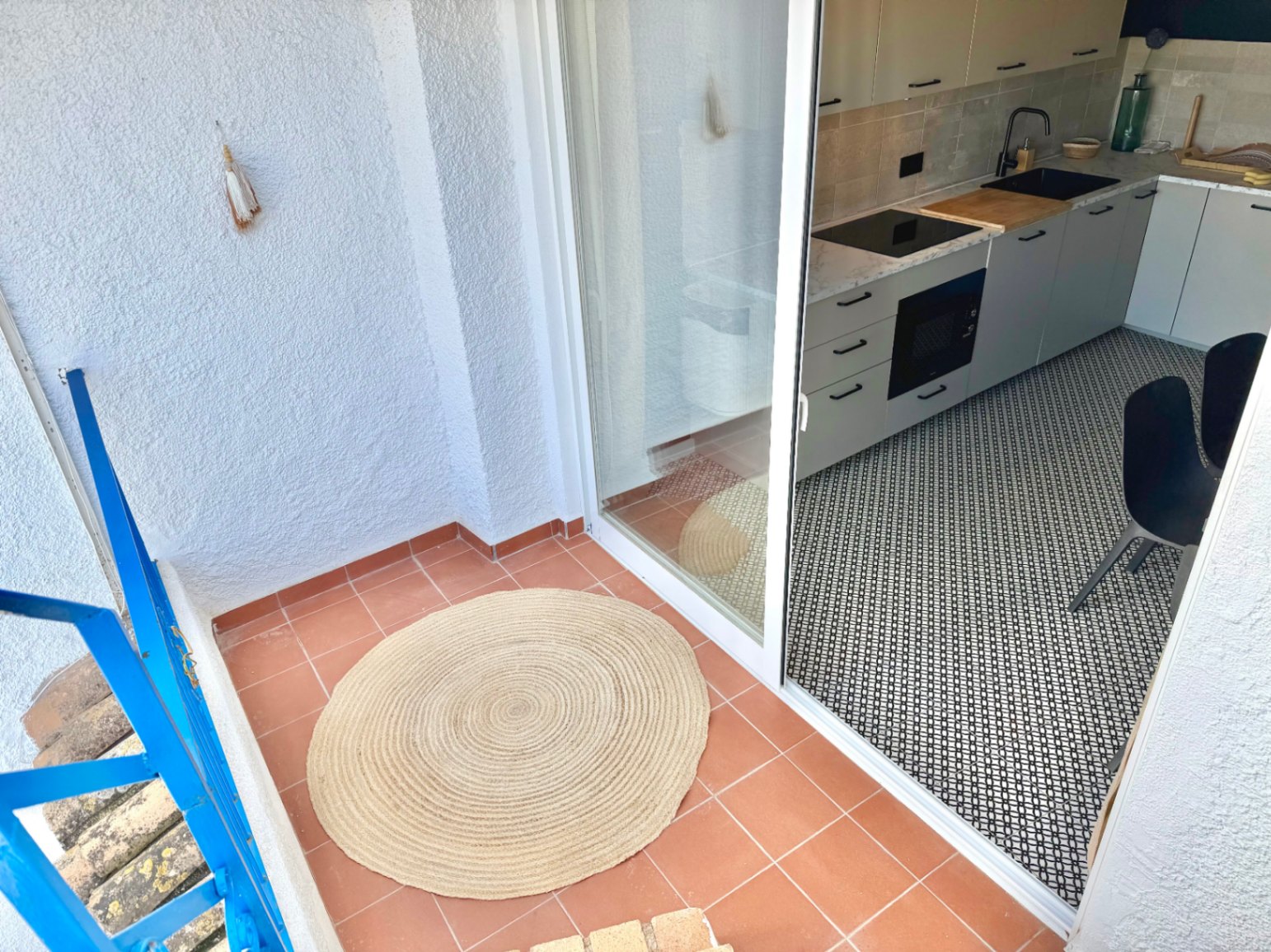 Terraza con suelo de terracota y acceso a cocina moderna con suelo geométrico.