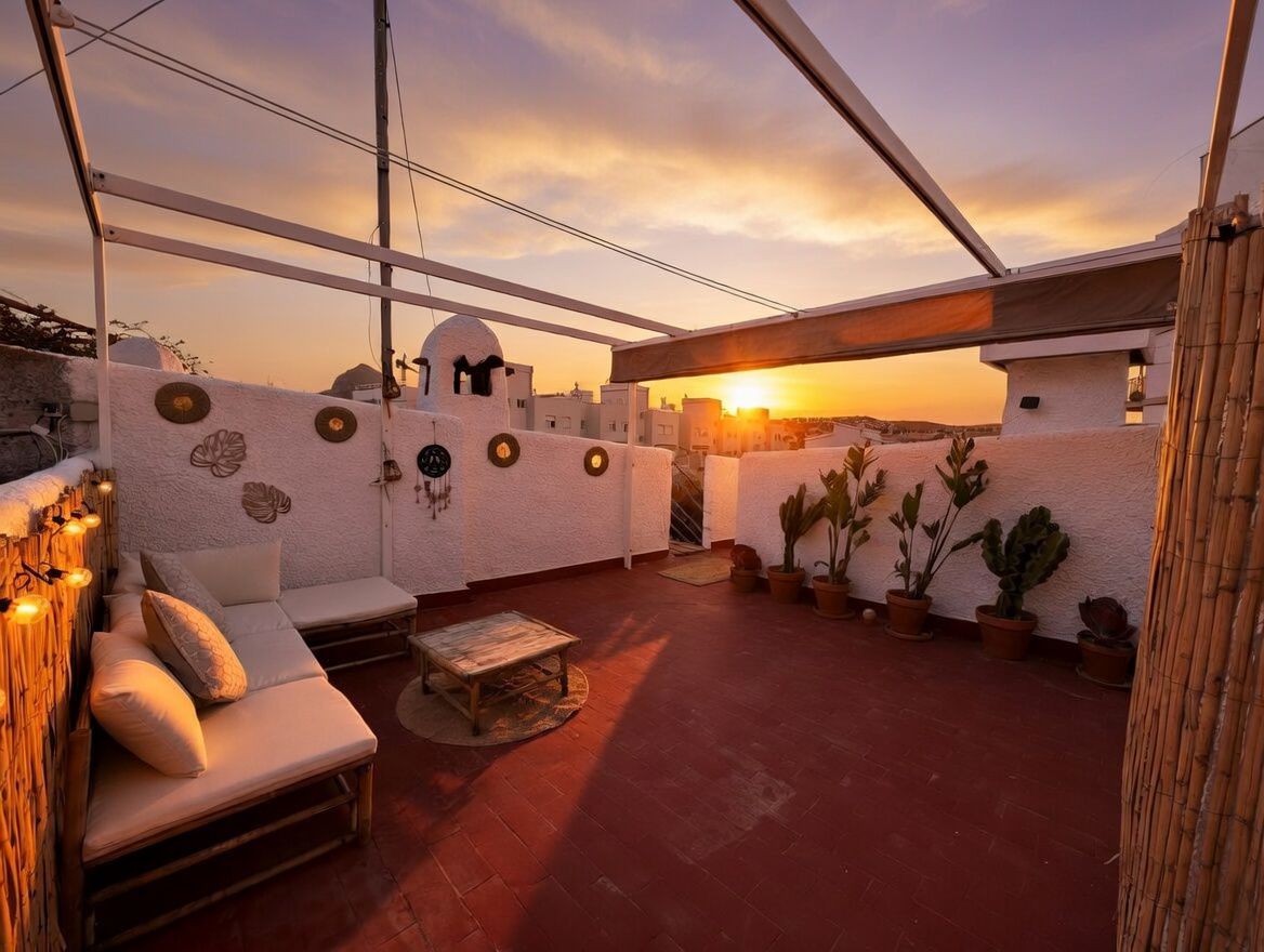 Terraza privada con suelo de terracota, decorada con plantas en macetas y mobiliario de bambú al atardecer.