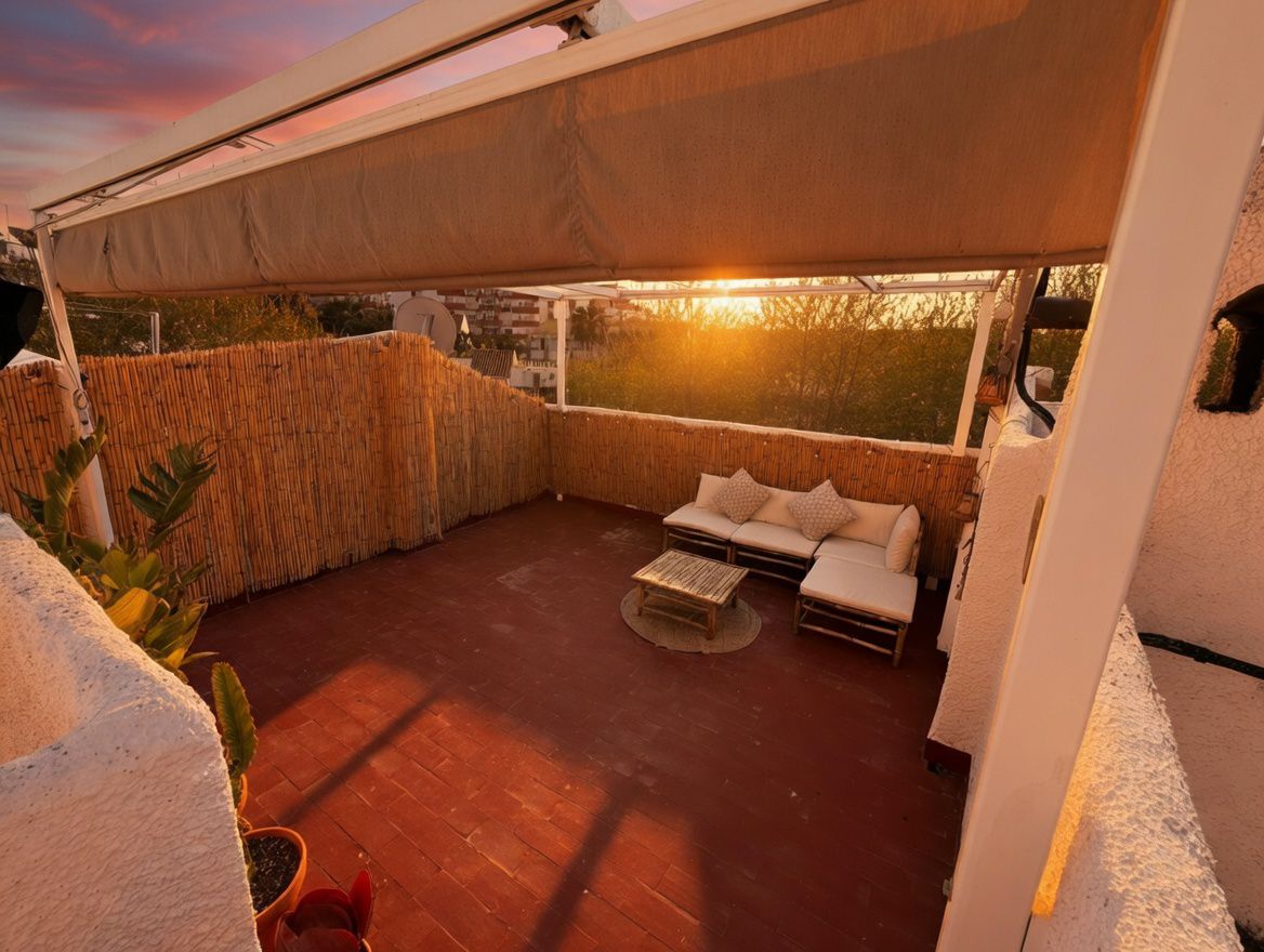 Terraza privada con toldo, suelo de baldosas rojas y cerramiento de bambú. Incluye mobiliario de exterior y vistas al atardecer.