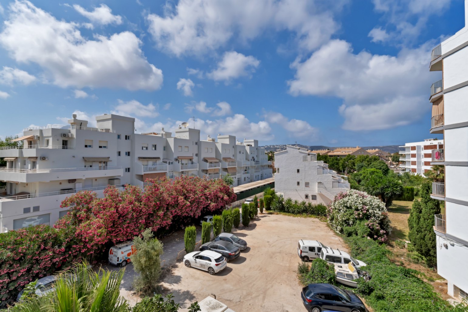 Vista elevada del aparcamiento comunitario rodeado de edificios blancos y exuberante vegetación en Jávea.