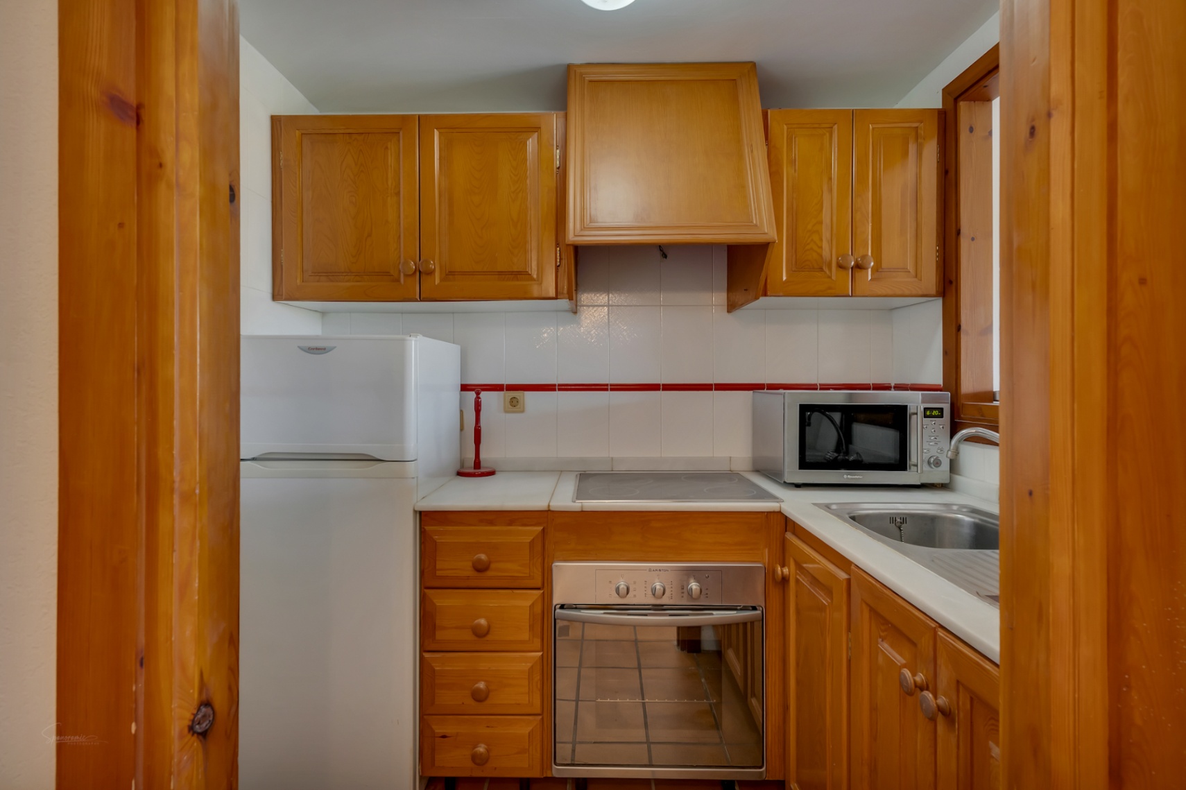 Cocina compacta con muebles de madera, electrodomésticos blancos y encimera clara.