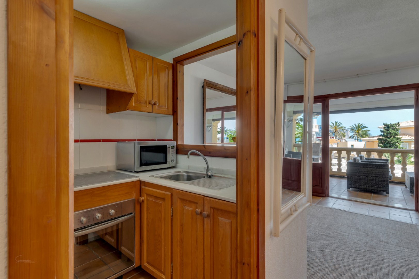 Cocina con muebles de madera y electrodomésticos modernos, con vista a la terraza acristalada.
